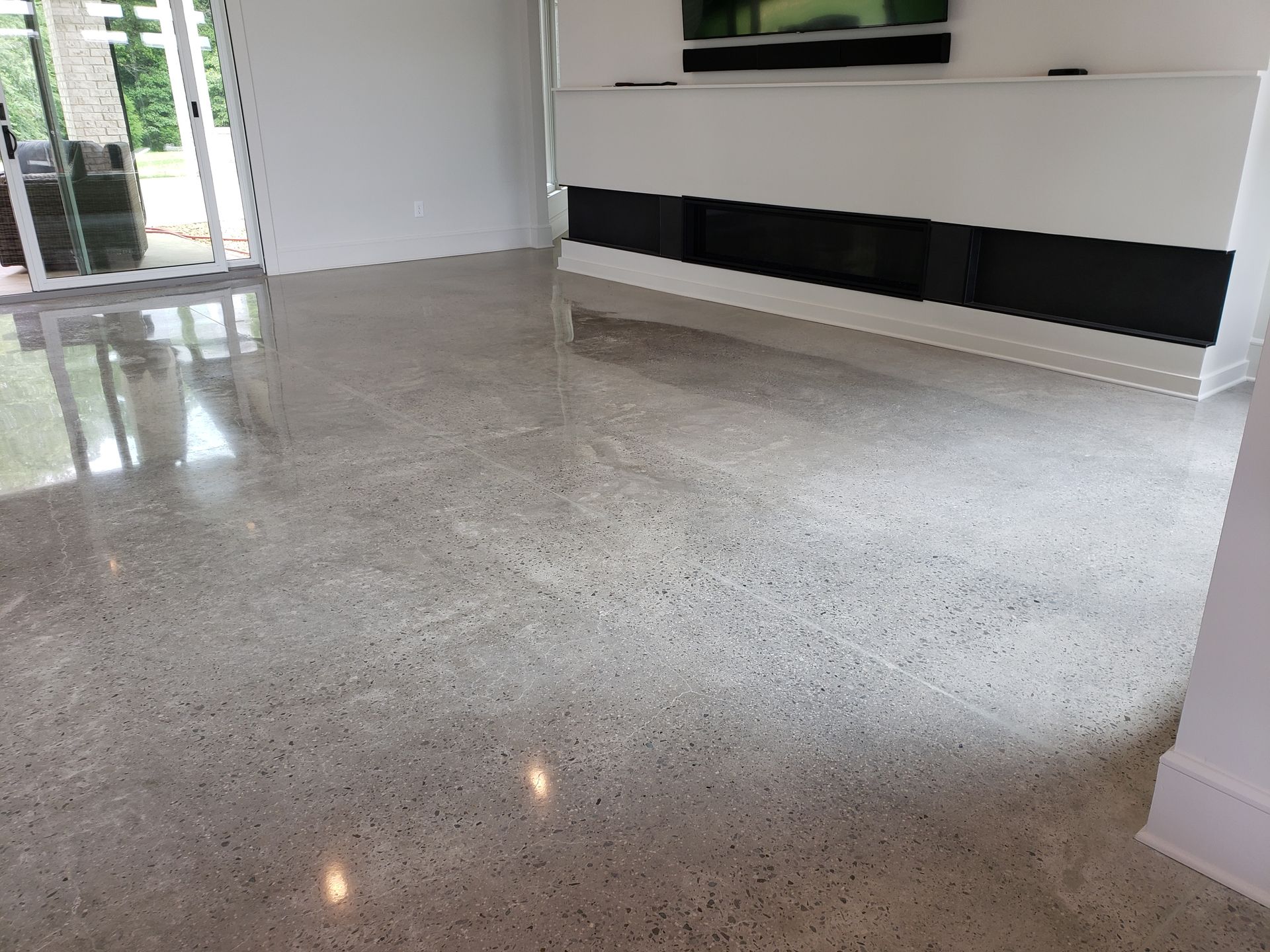 Polished gray concrete floor reflecting light, in a modern living room with white walls and fireplace.