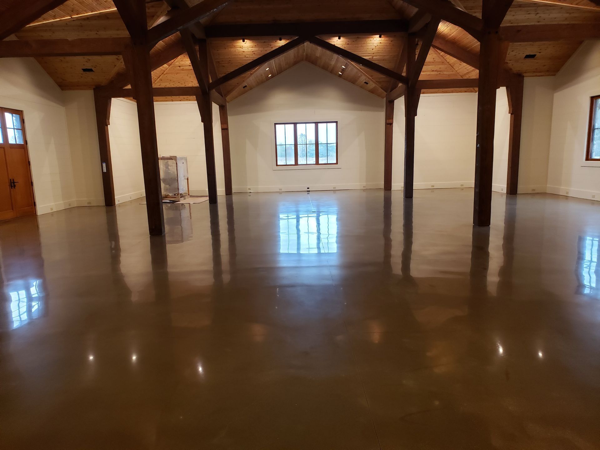 Spacious interior with polished concrete floor, exposed wooden beams, and neutral walls. Sunlight reflects off the floor.