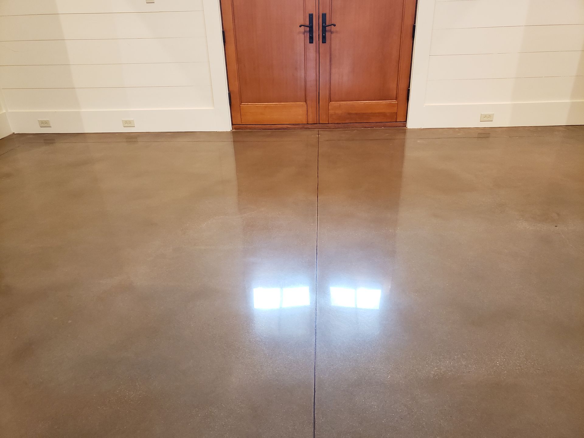 Polished concrete floor in front of brown double doors. White horizontal planks line the wall above the floor.