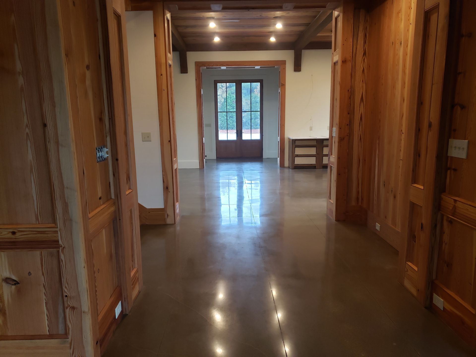 Hallway with polished concrete floor and wooden walls and trim. Doors lead to other rooms; natural light streams in.