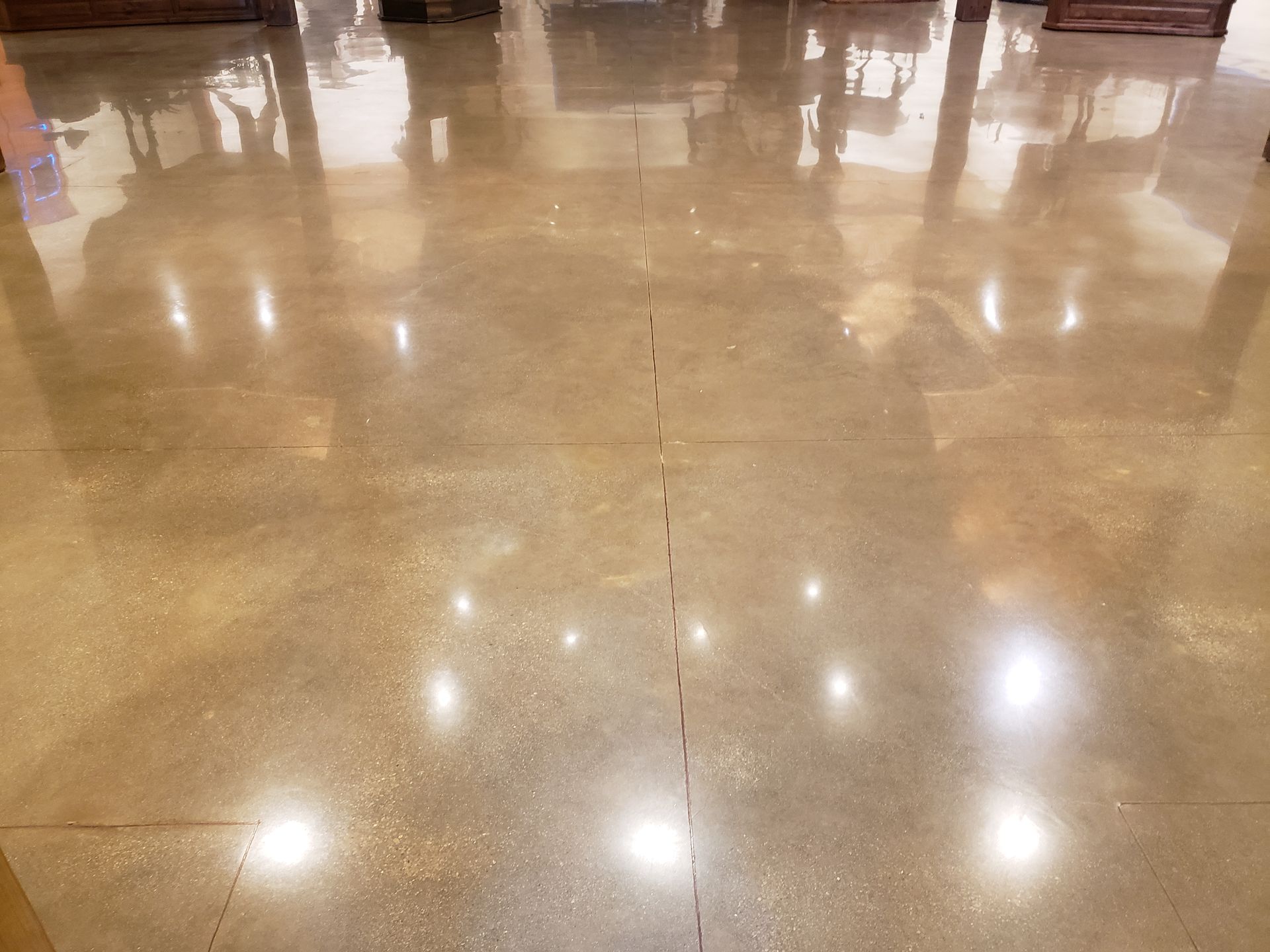 Polished concrete floor reflecting overhead lights and blurred architectural elements in a commercial space.