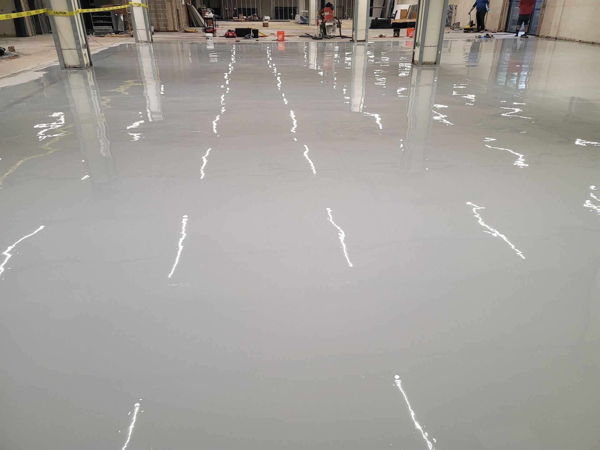 Gray epoxy floor coating being applied in an industrial space. Several workers are visible in the background.