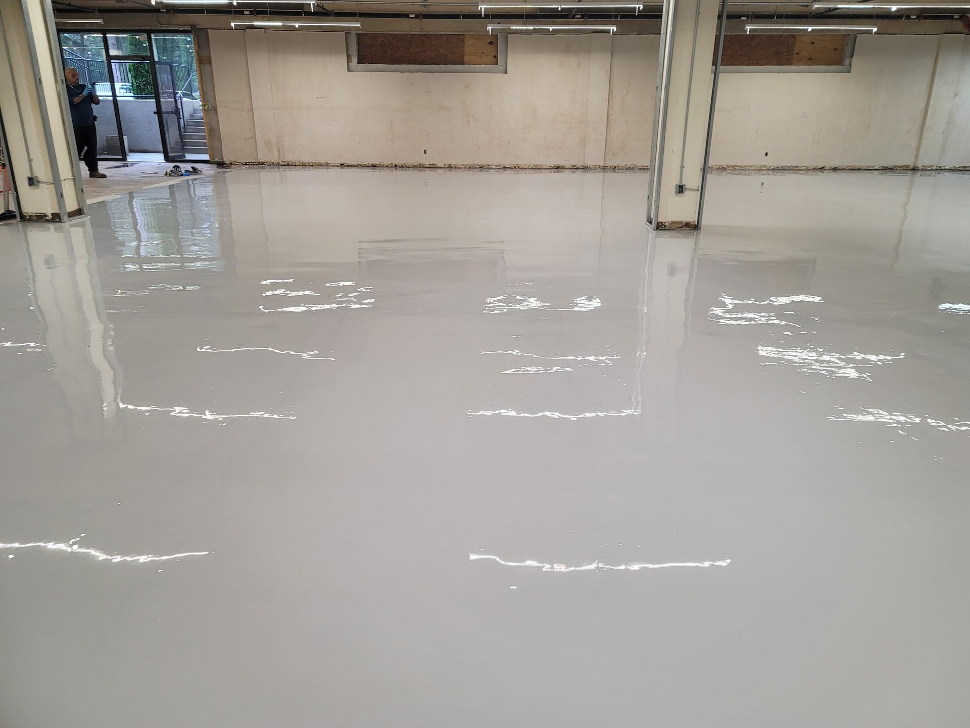 A spacious, empty room with a glossy, light gray epoxy floor. A person stands by an open doorway.