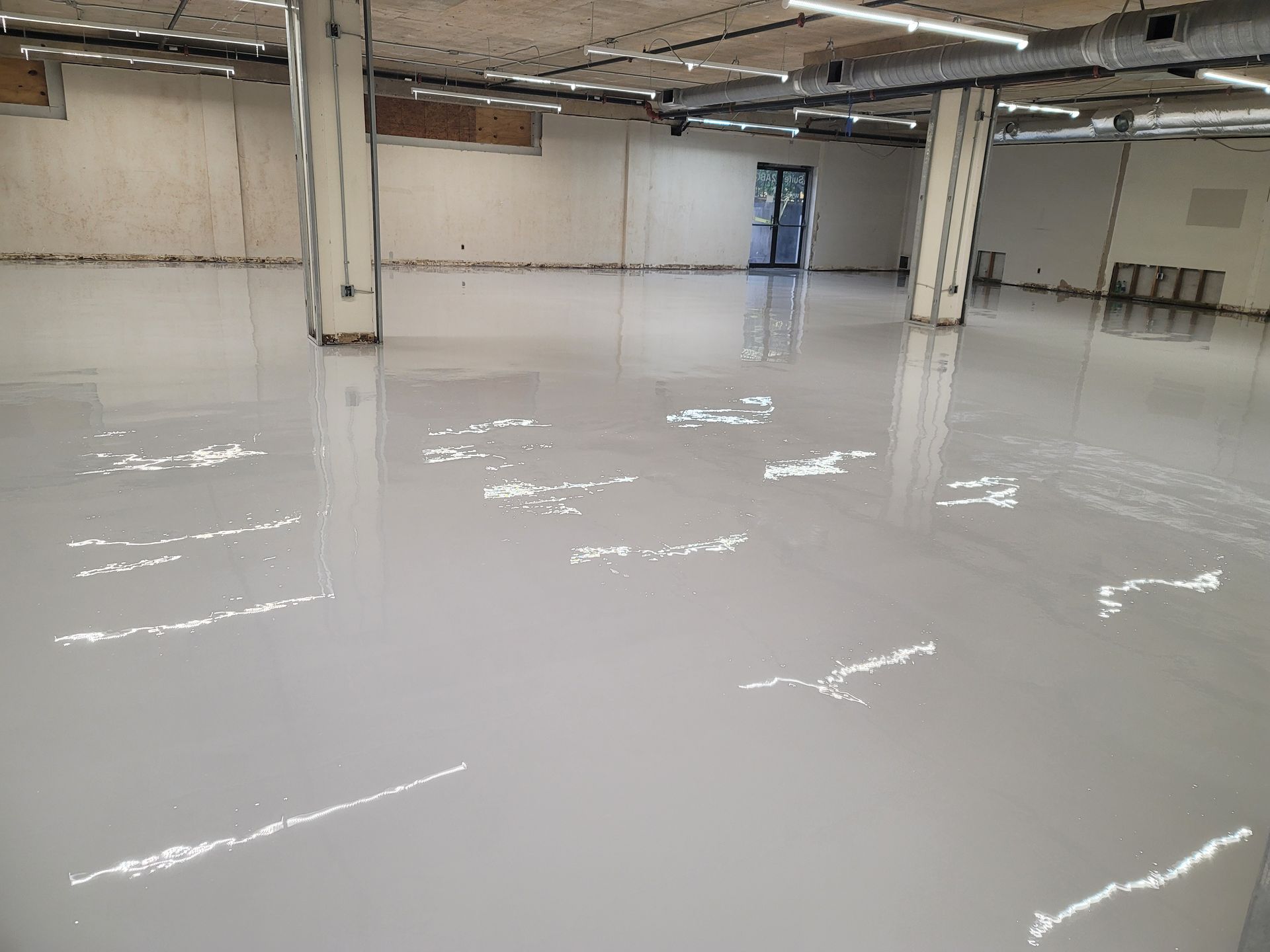 Spacious interior with a newly poured, light gray epoxy floor. The space appears empty, with support columns and exposed ceiling.