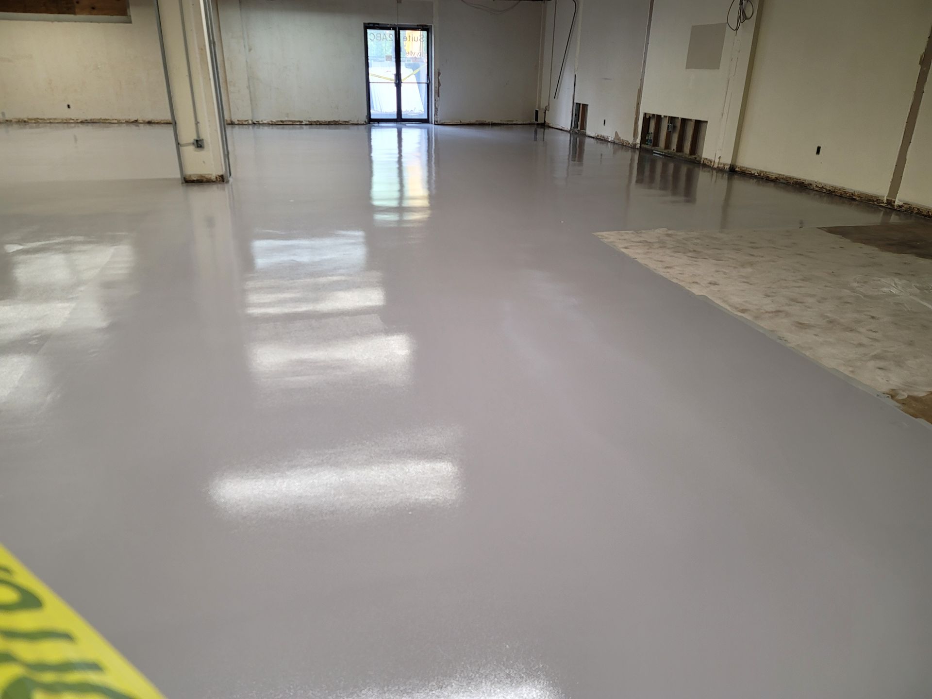 A large room with a newly coated, shiny, light-grey floor. A glass door is at the back of the room.