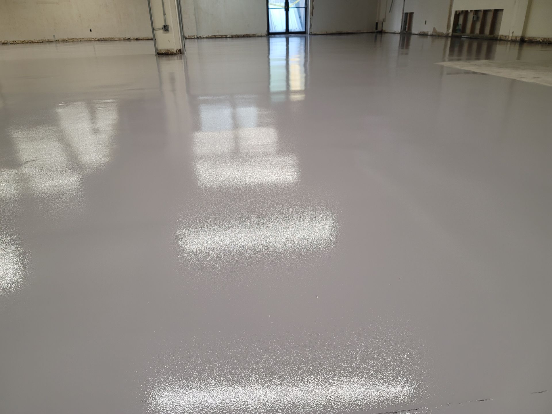 Gray, glossy epoxy floor reflecting interior windows and light. Empty industrial or commercial space.