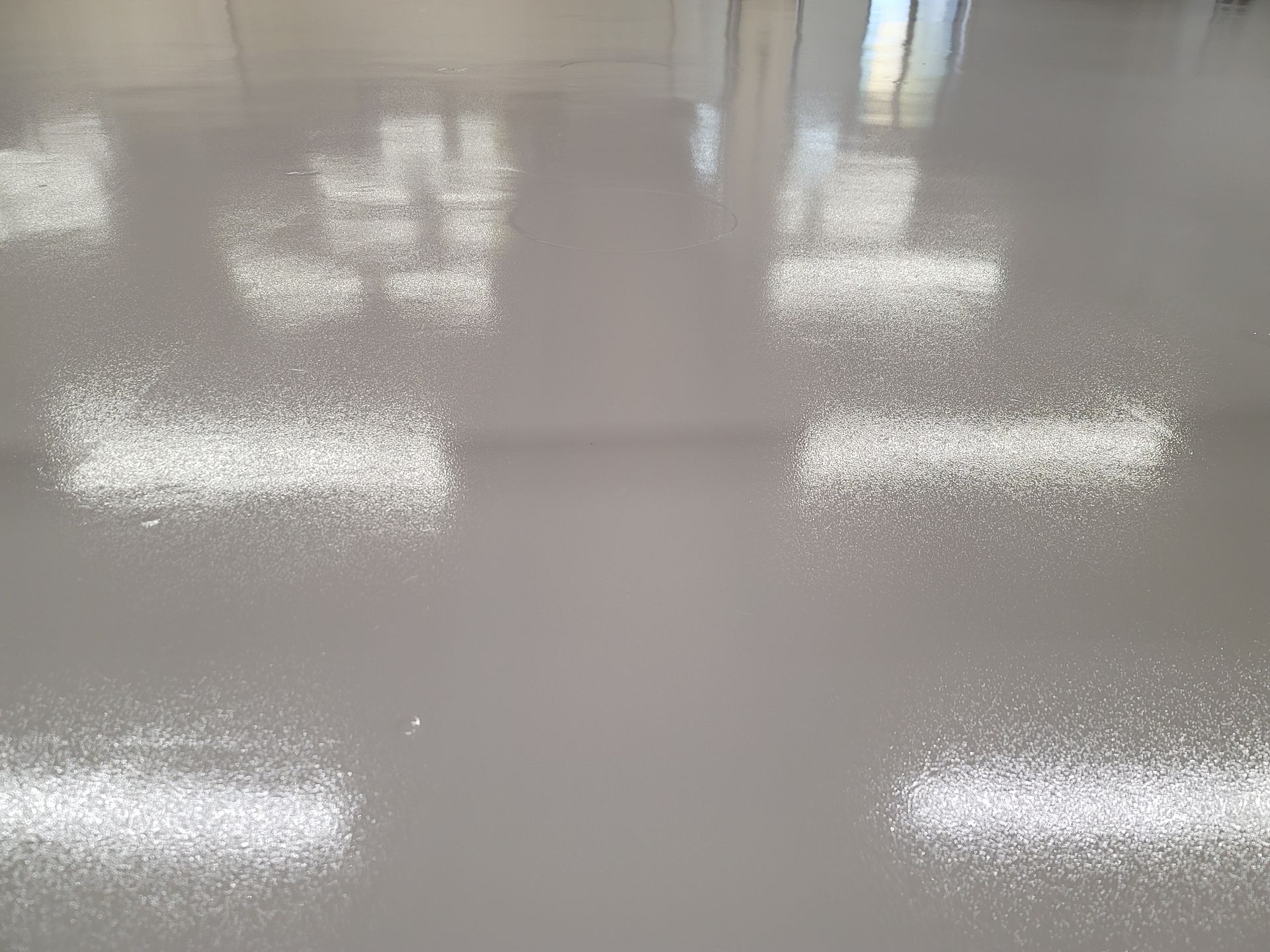 Shiny, gray floor reflecting bright rectangular lights and a window, creating a blurred reflection.