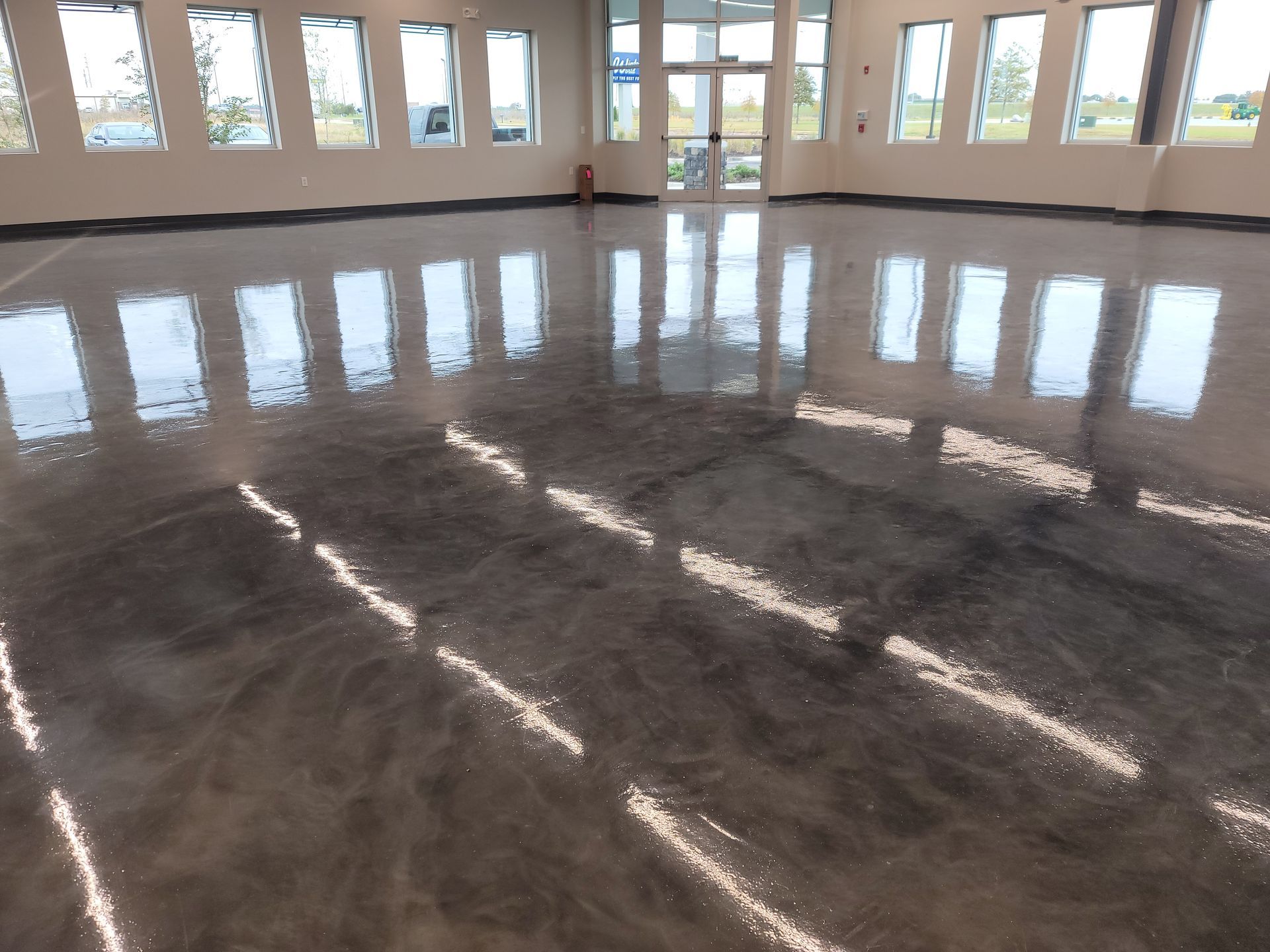 Shiny, reflective gray floor in a building with many windows. Sunlight casts bright streaks across the floor.