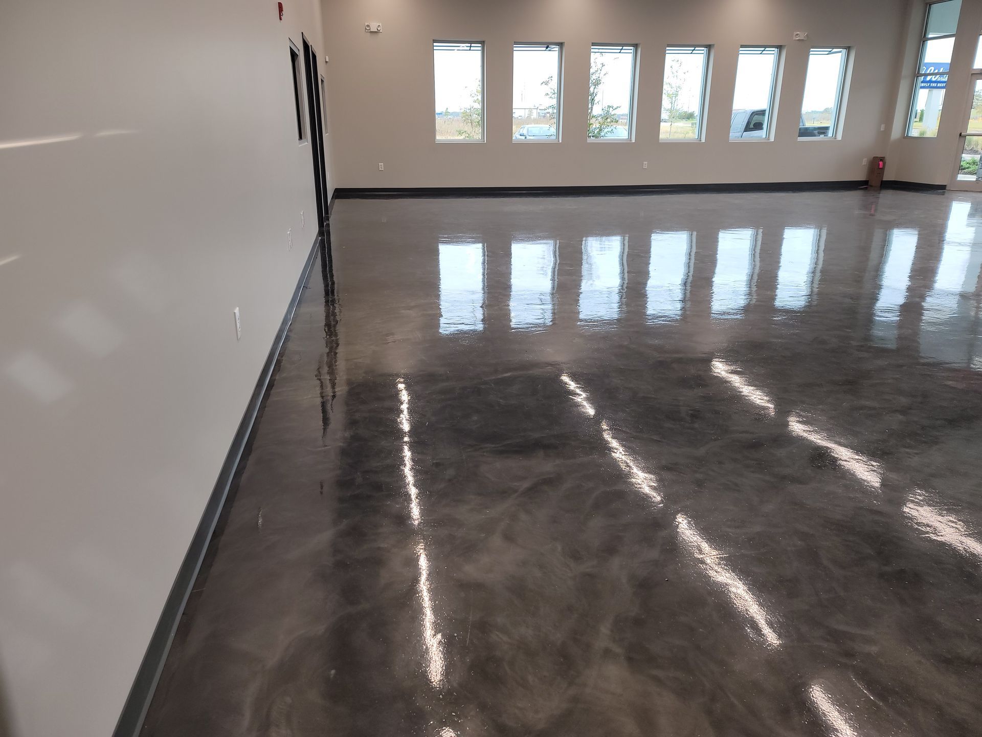 Shiny, polished concrete floor reflecting natural light from the windows in an empty room with gray walls.