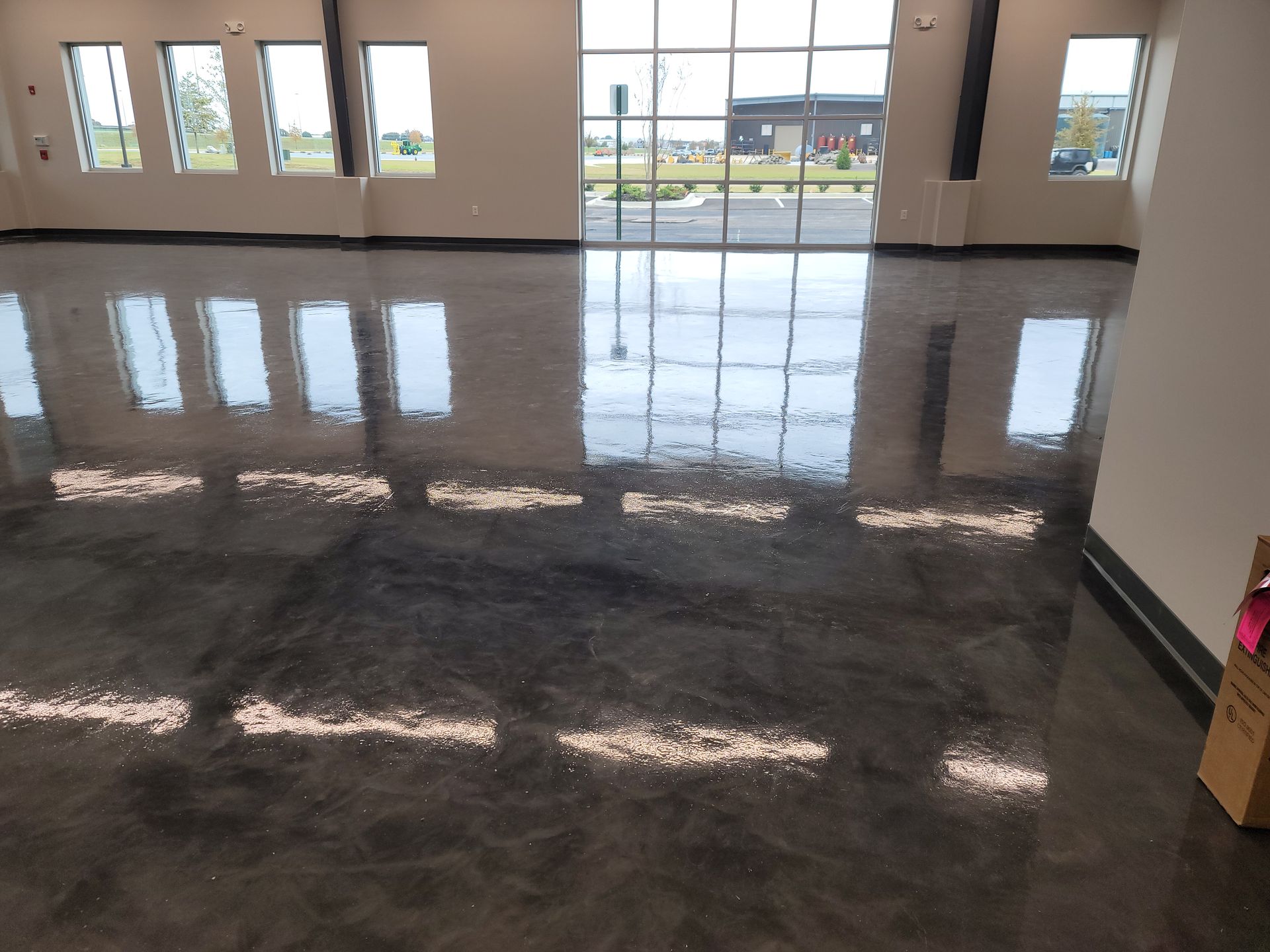 Glossy, dark gray epoxy floor reflects sunlight from windows in a spacious interior. The space appears empty.