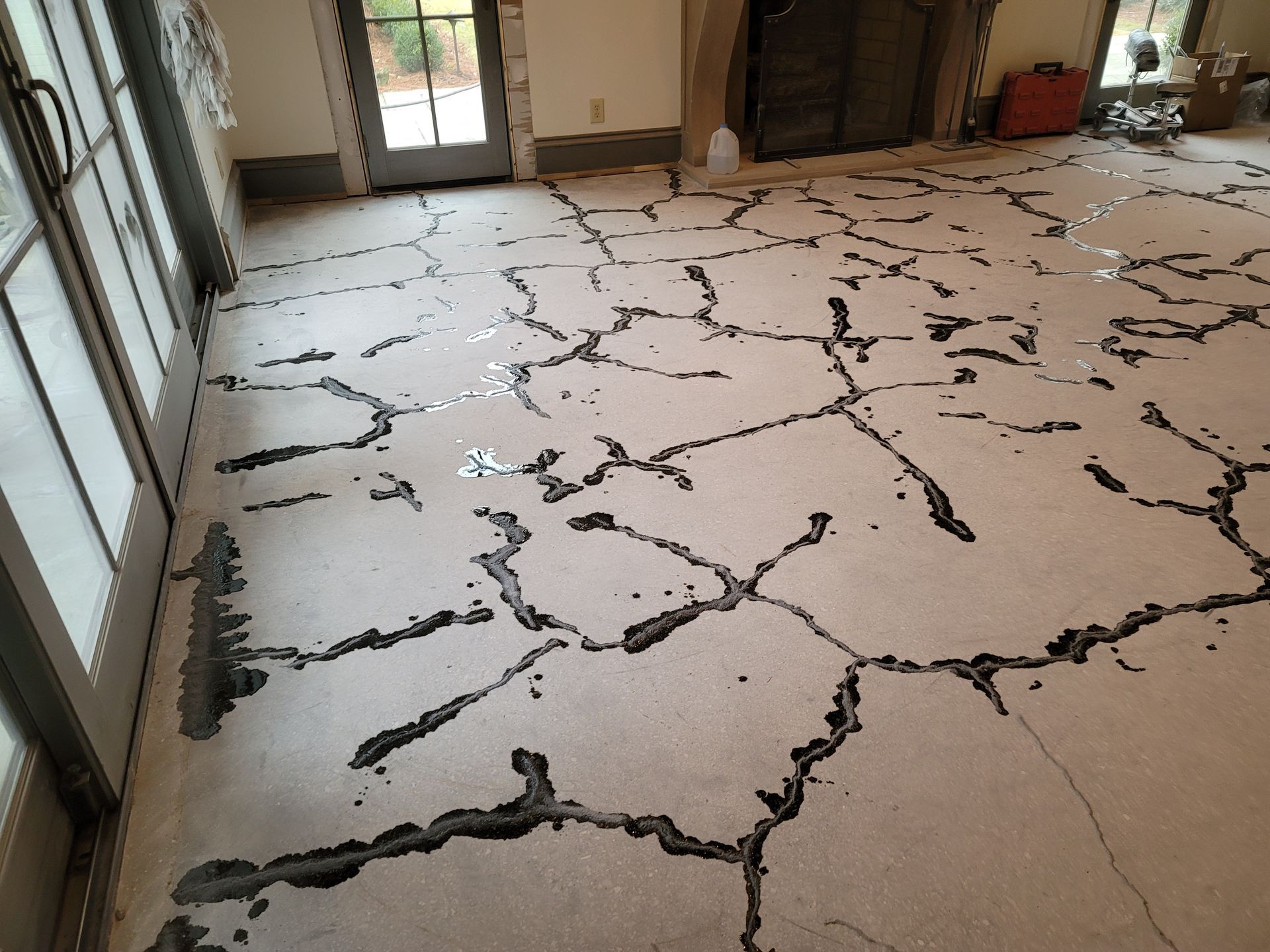 Concrete floor extensively cracked and damaged. The cracks are filled with dark material, covering a large area of a room.