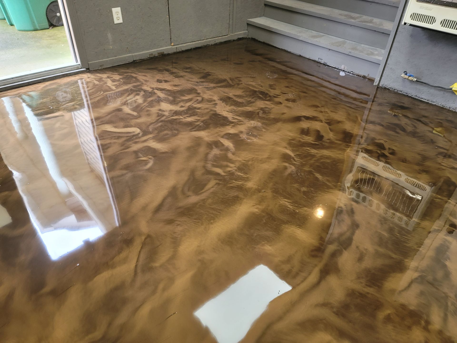 Metallic epoxy flooring in shades of brown and gold, reflecting light. The flooring is indoors, likely a garage or workshop.