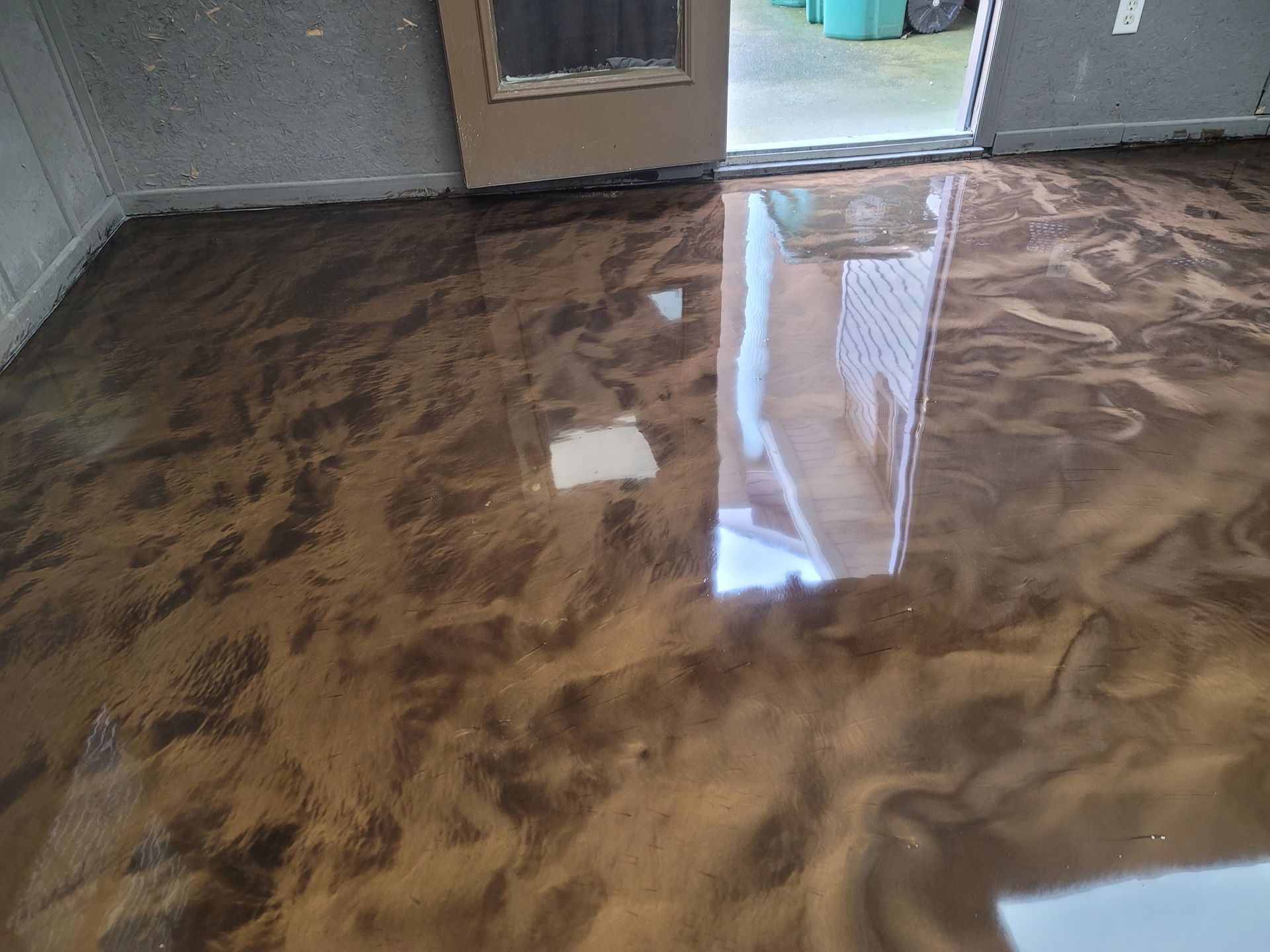Metallic epoxy flooring in shades of brown and bronze, reflecting the open doorway and surroundings of a room.
