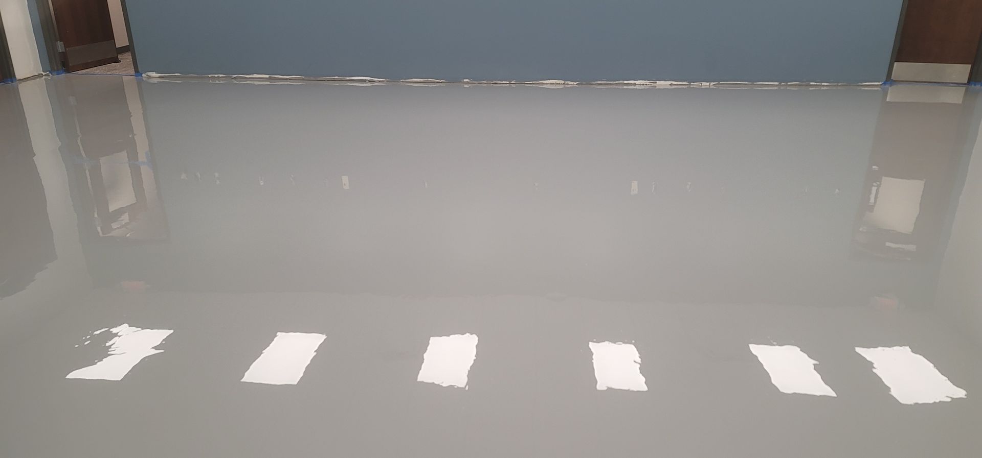 A gray, glossy floor reflects the room's walls and ceiling, with bright rectangular reflections scattered across the surface.