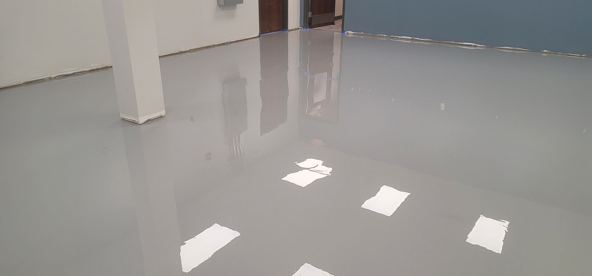 A glossy, gray epoxy floor reflecting bright light.  A white support column and walls are visible in a commercial space.