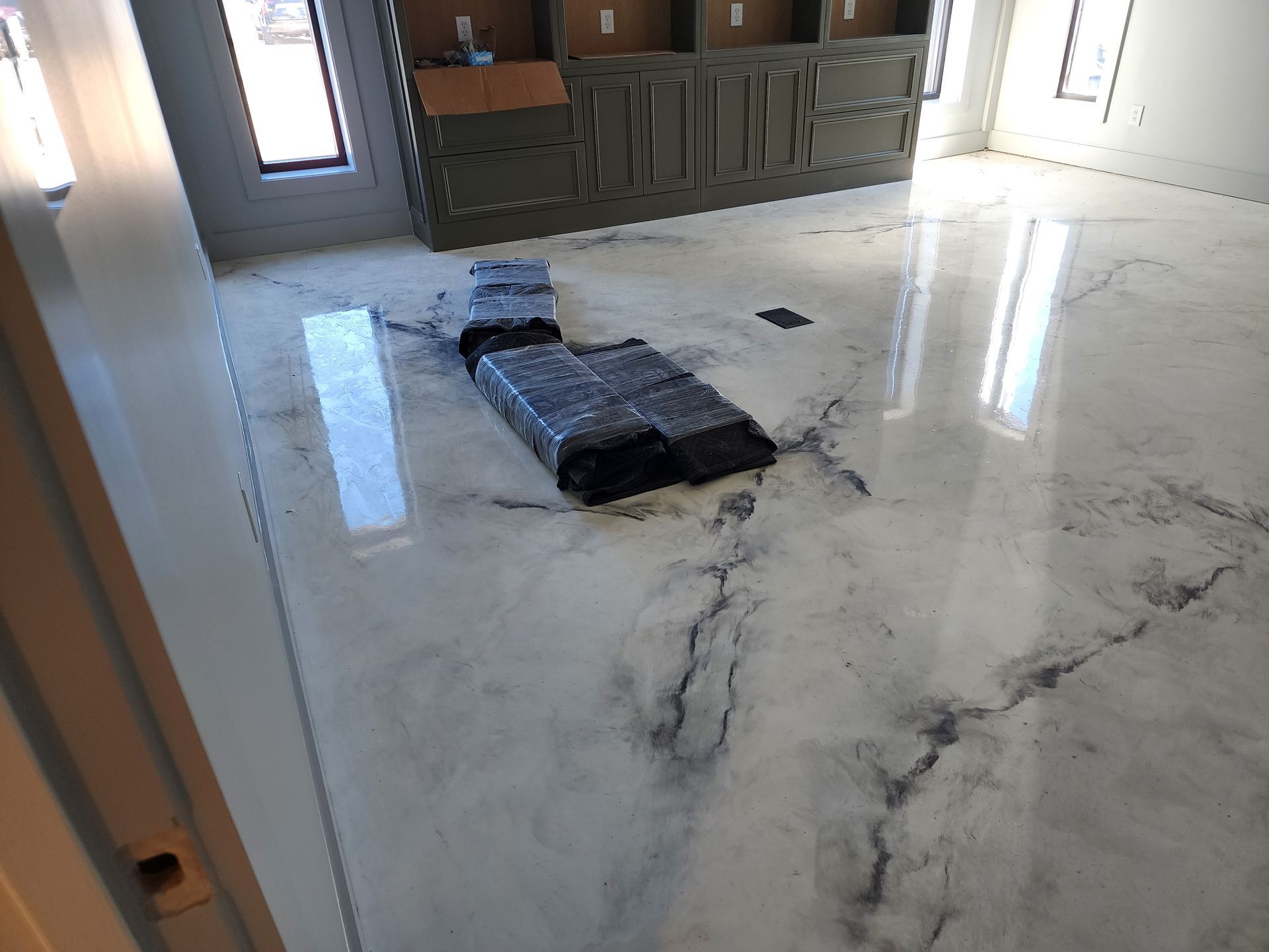 Glossy, white floor with dark veins. A dark, rolled-up mat and cabinets are in the background, reflecting light from windows.