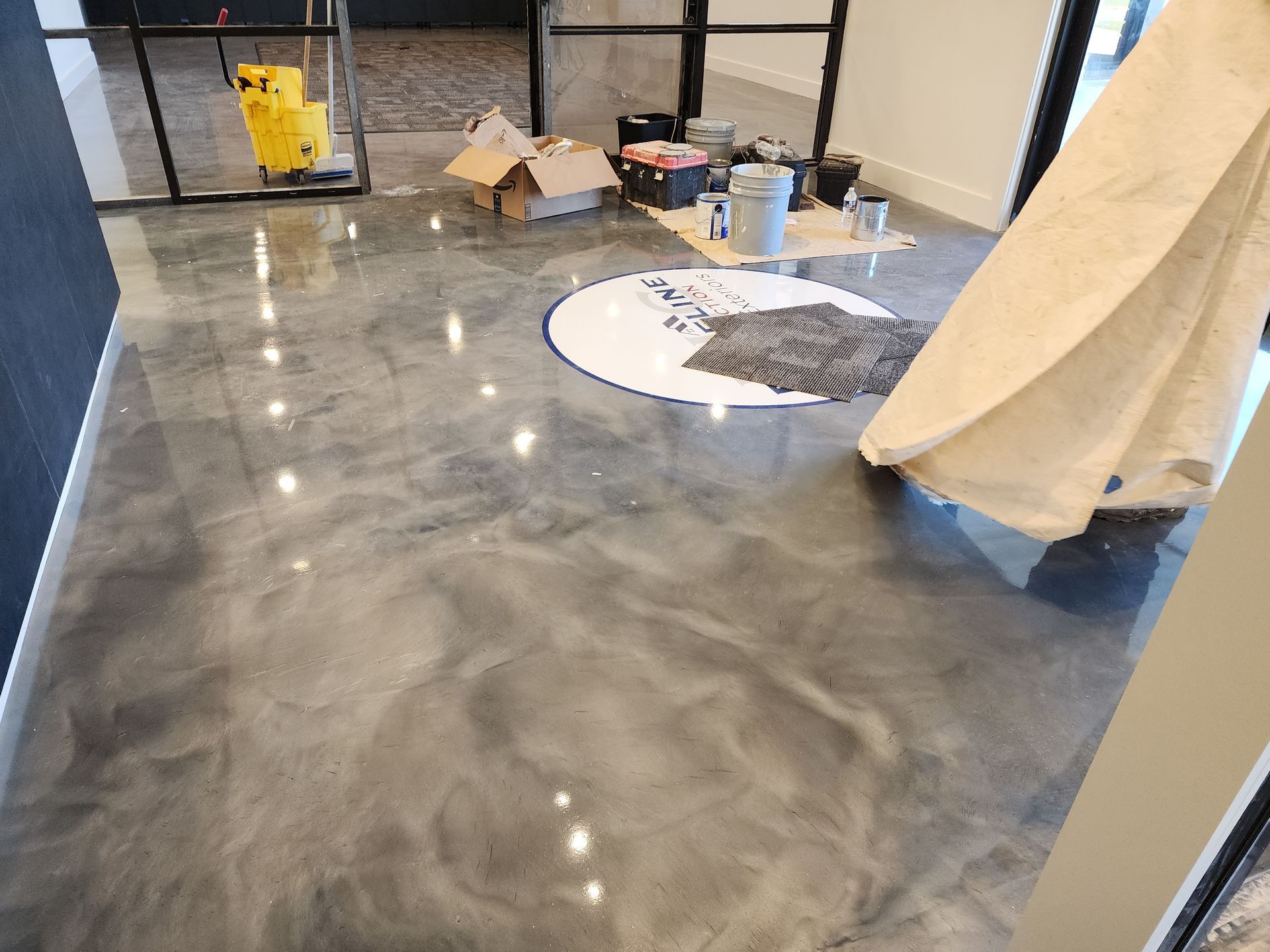 Shiny gray epoxy flooring in an interior space, with a mop bucket and painting supplies visible.