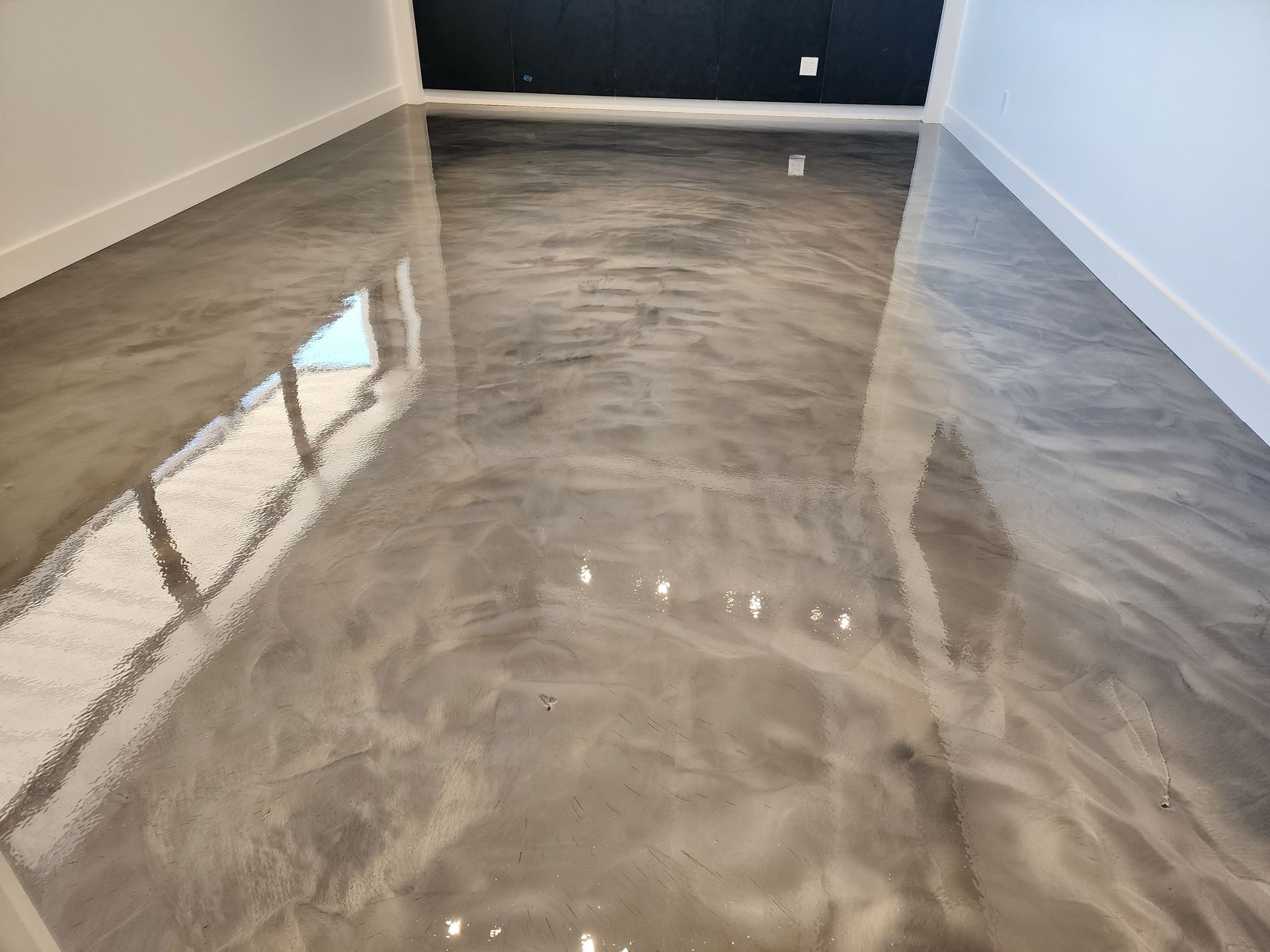 Metallic silver epoxy flooring in a room reflecting light. White baseboards and a dark wall in the background.