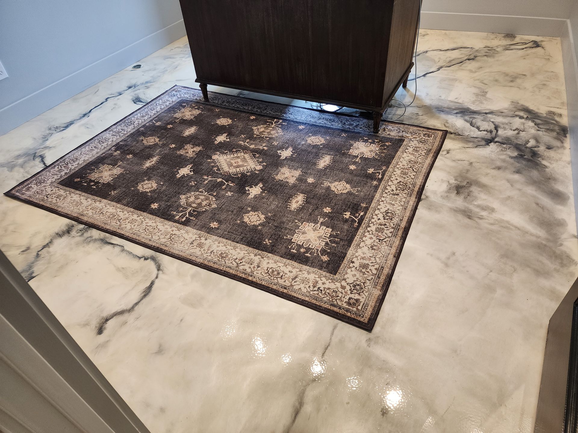 A dark rug sits on a marble-patterned epoxy floor in a room with dark cabinetry.