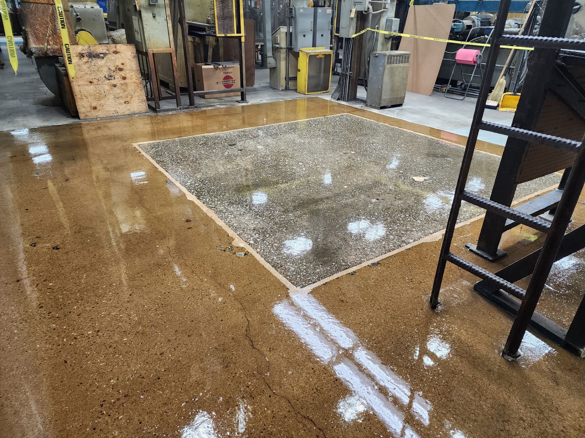Brown and tan industrial floor with water pooling on it, with a ladder in the right corner. The floor is enclosed in a square bordered pattern.