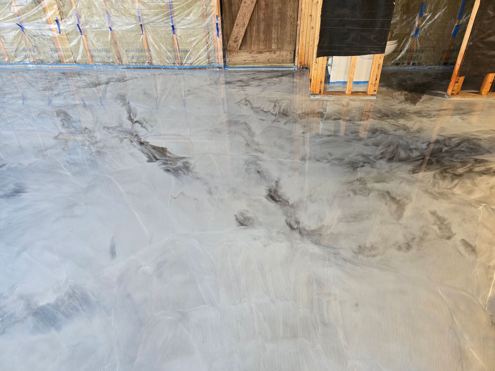 Metallic epoxy floor in shades of silver and gray in a new construction setting with exposed insulation and framing.