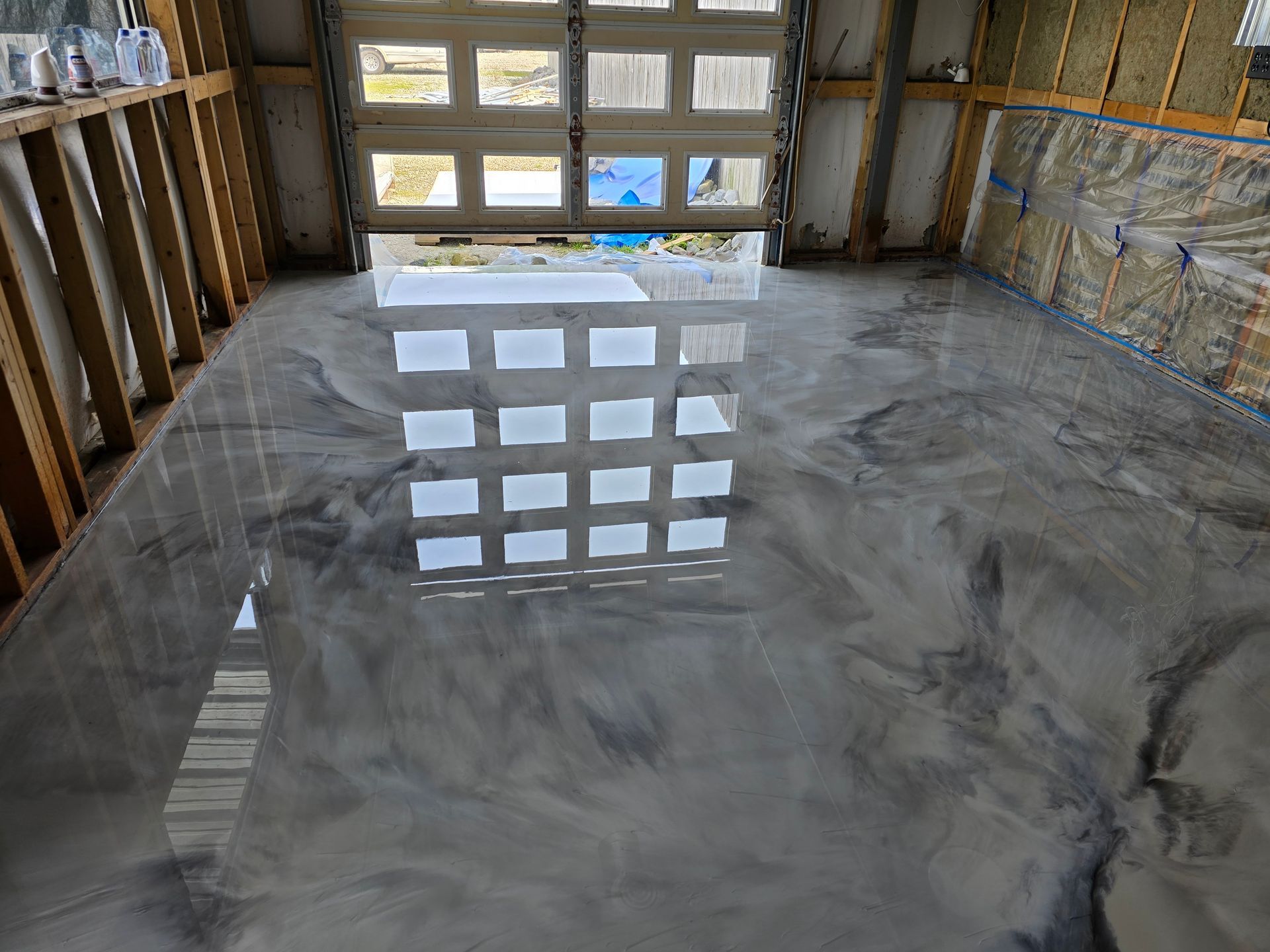 Shiny, metallic epoxy garage floor with reflections of the garage door. Gray and silver tones throughout.