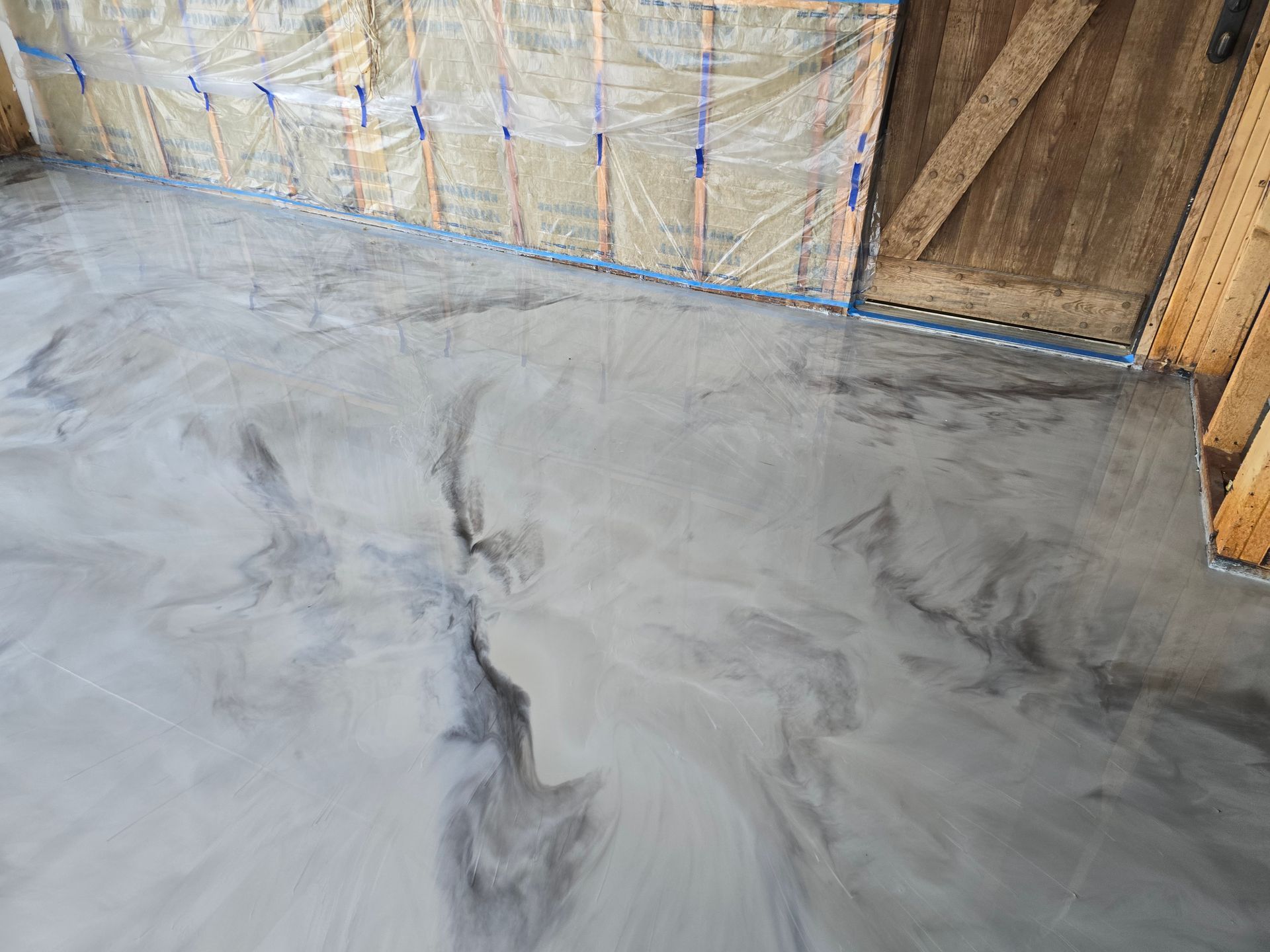 Metallic epoxy floor with swirling gray and silver patterns, in a room with wooden walls and a door.