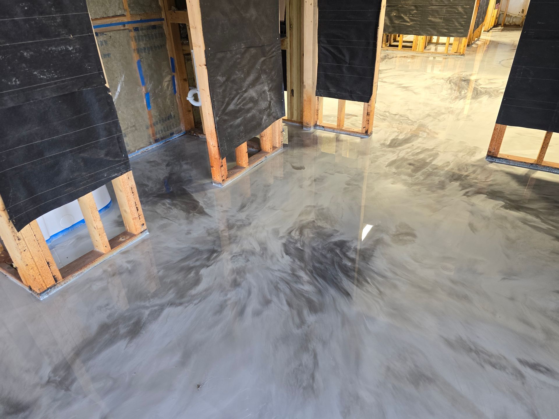 Metallic epoxy floor with swirls of silver and gray in a room under construction. Wooden framing and black barriers line the walls.