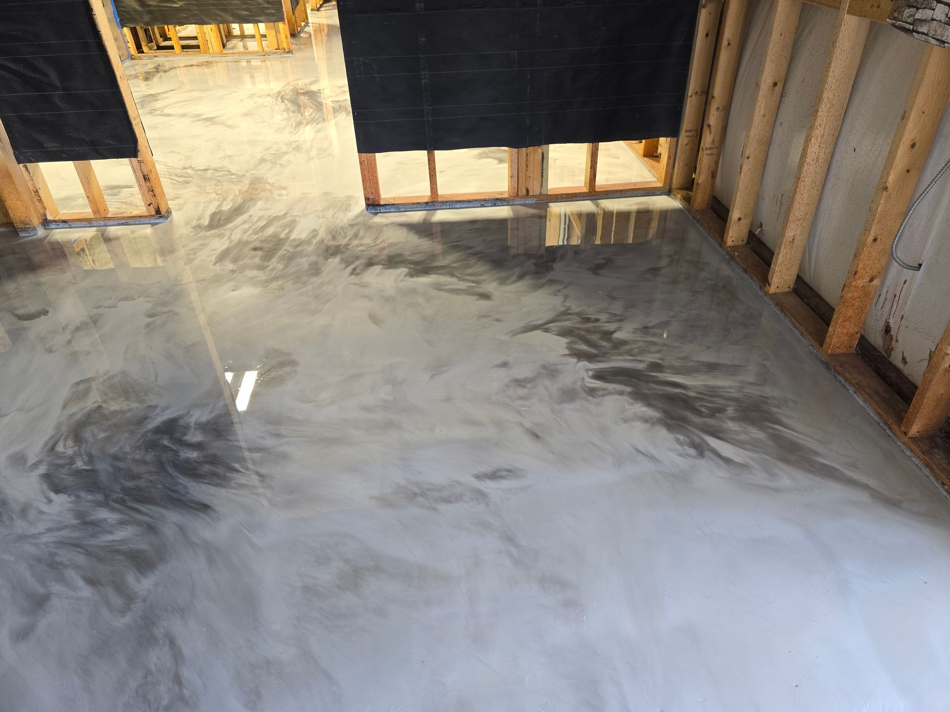 Metallic gray epoxy flooring in a room with wooden framing. The reflective surface creates a swirled pattern.