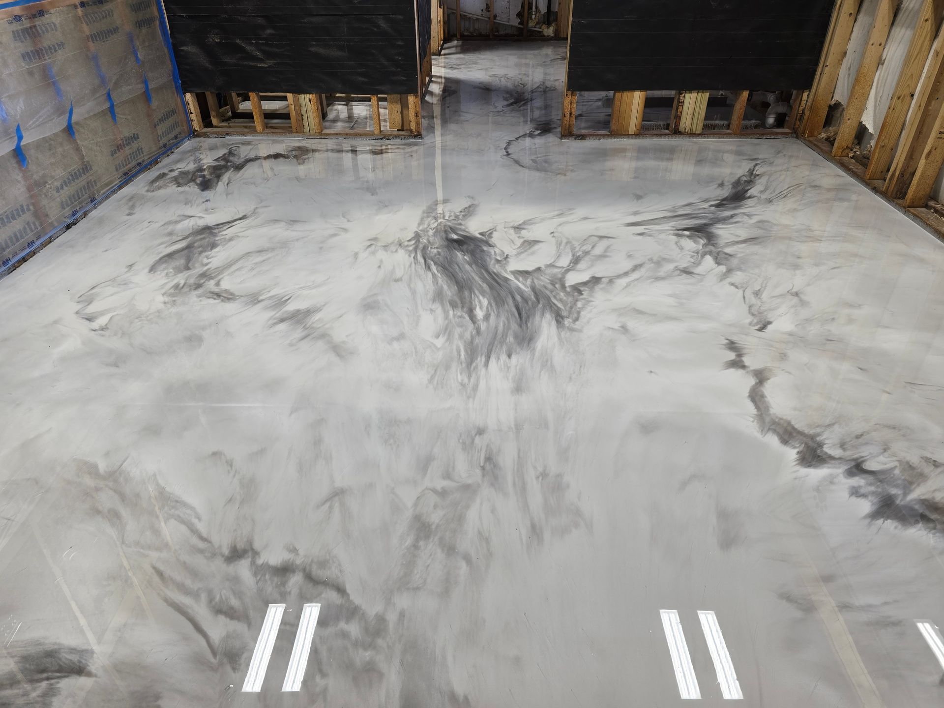 Metallic epoxy flooring in a room under construction; silver and gray swirls, wood framing visible.