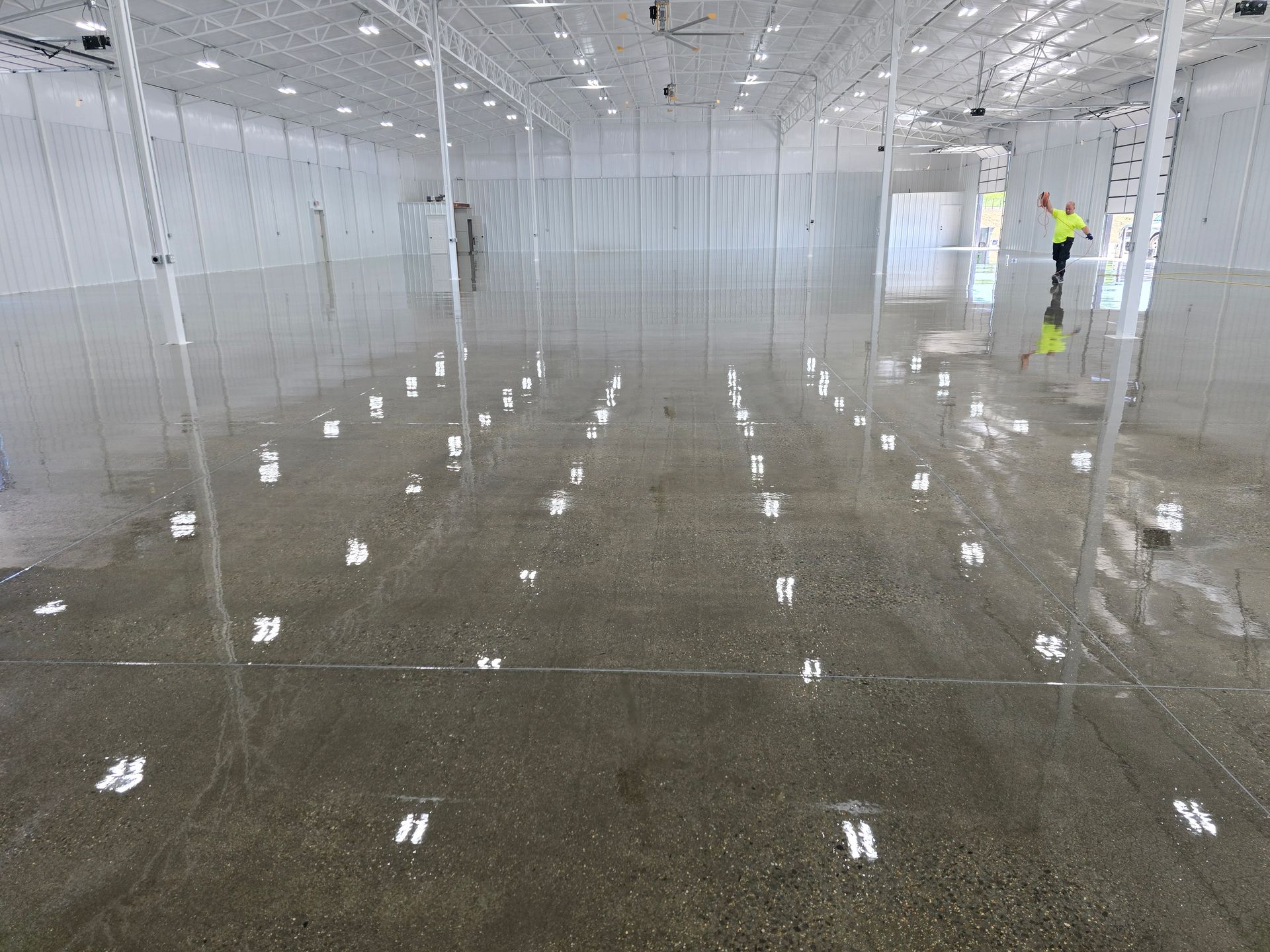 Wide shot of a large, empty, industrial-style room.  The floor is wet, and white markers are placed on it in rows. A worker stands in the distance.