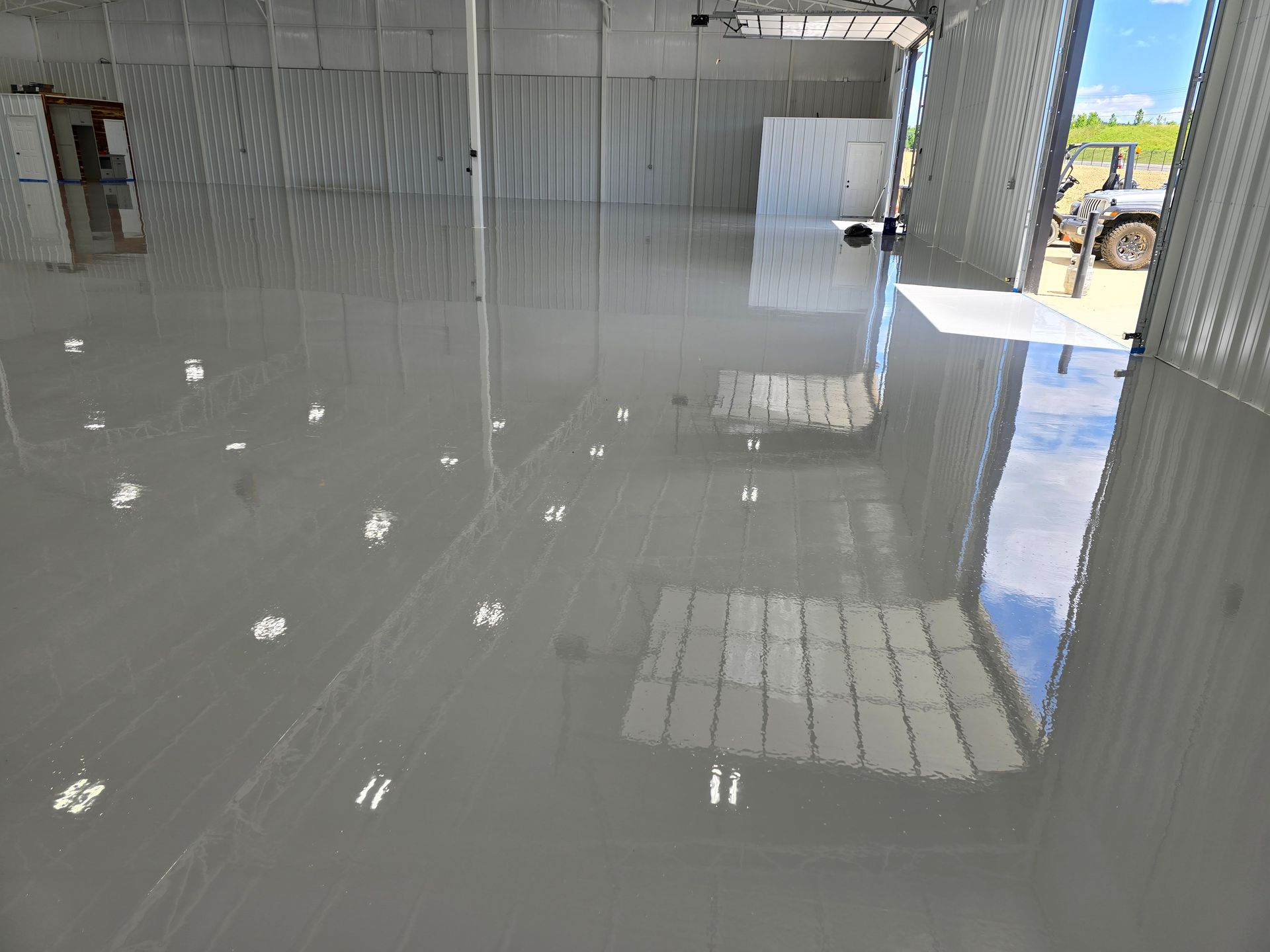 A shiny gray epoxy floor inside a large warehouse with reflections of the building's features and sunlight.