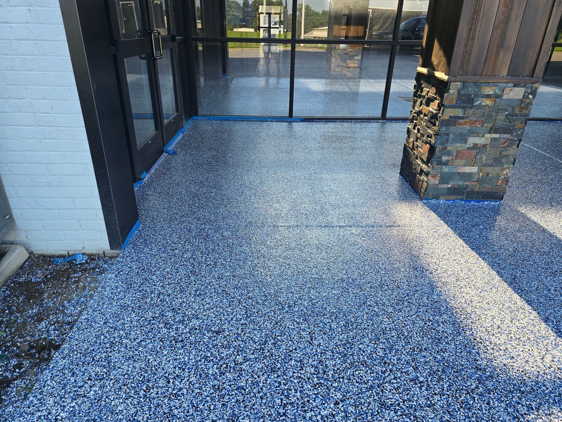 A blue and white speckled epoxy floor outside a building entrance with glass doors and a stone pillar.