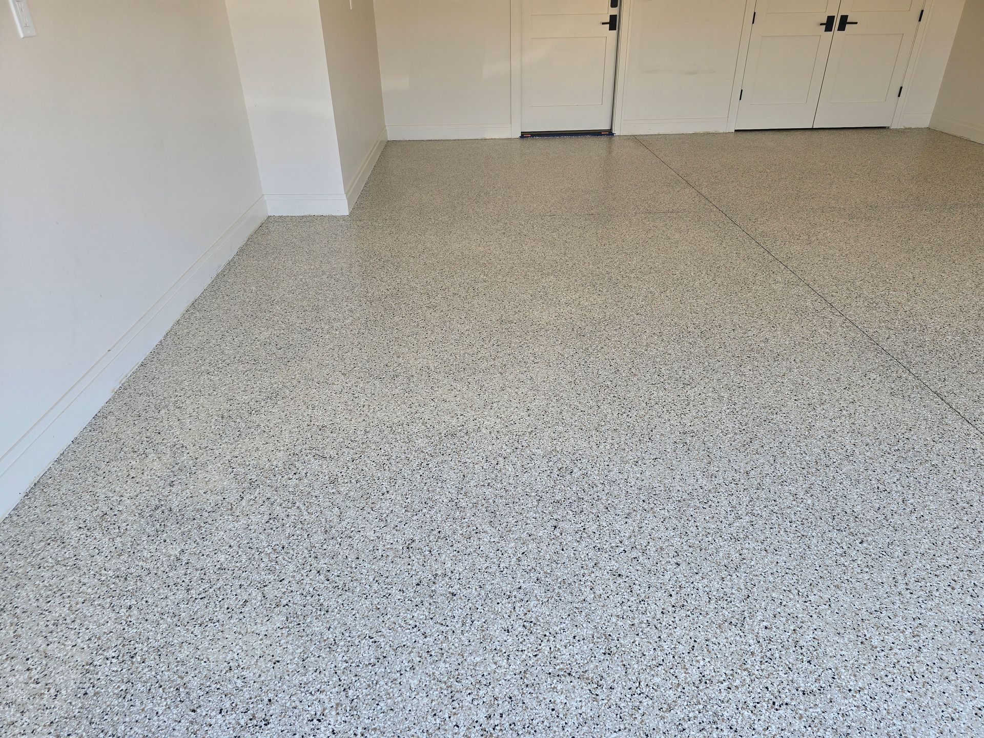 A garage floor with a speckled, light gray and dark gray epoxy coating. The walls are white.