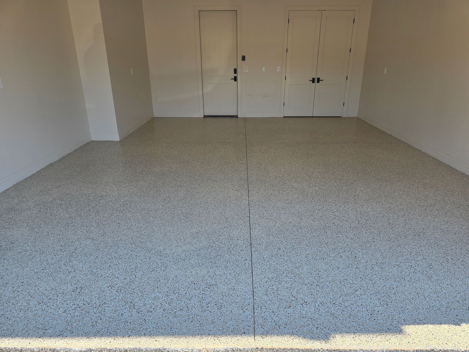 A newly finished garage with a speckled, light gray floor, two white doors, and light-colored walls.