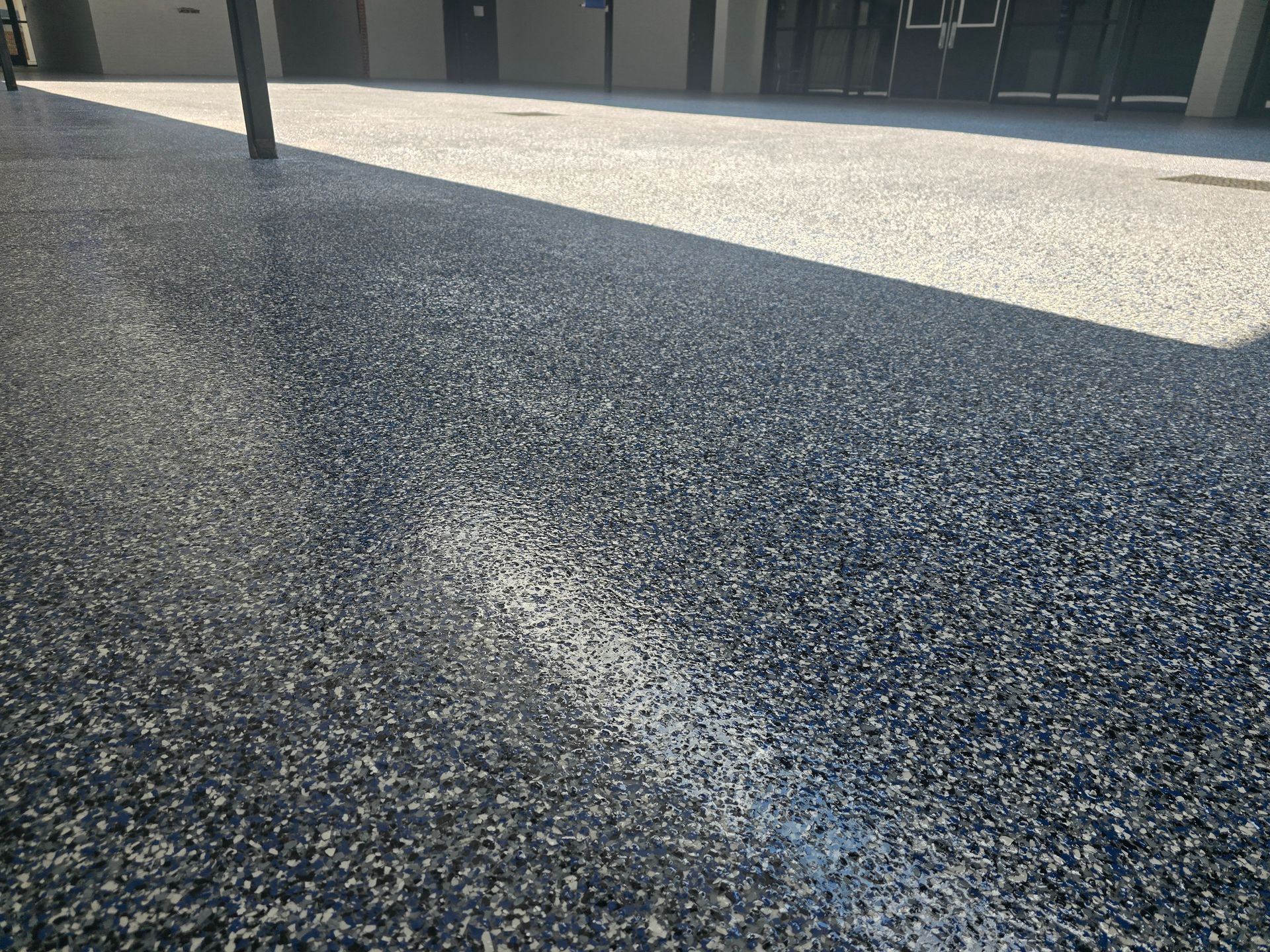 A speckled, dark blue and gray concrete outdoor surface. The area is partially shaded and leads to a building.