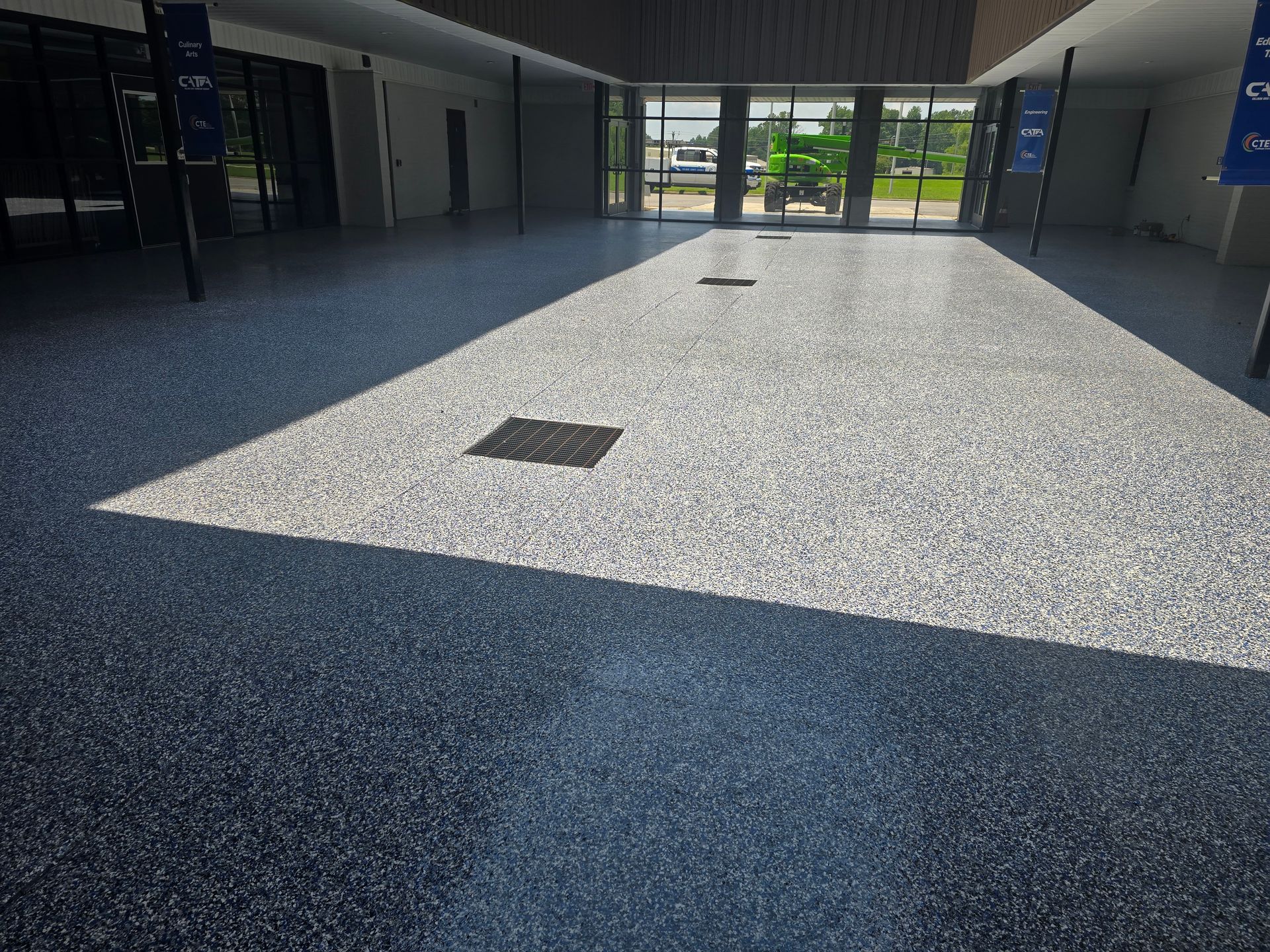 A bright, spacious room with a speckled floor and a shadow cast across it from a large window.