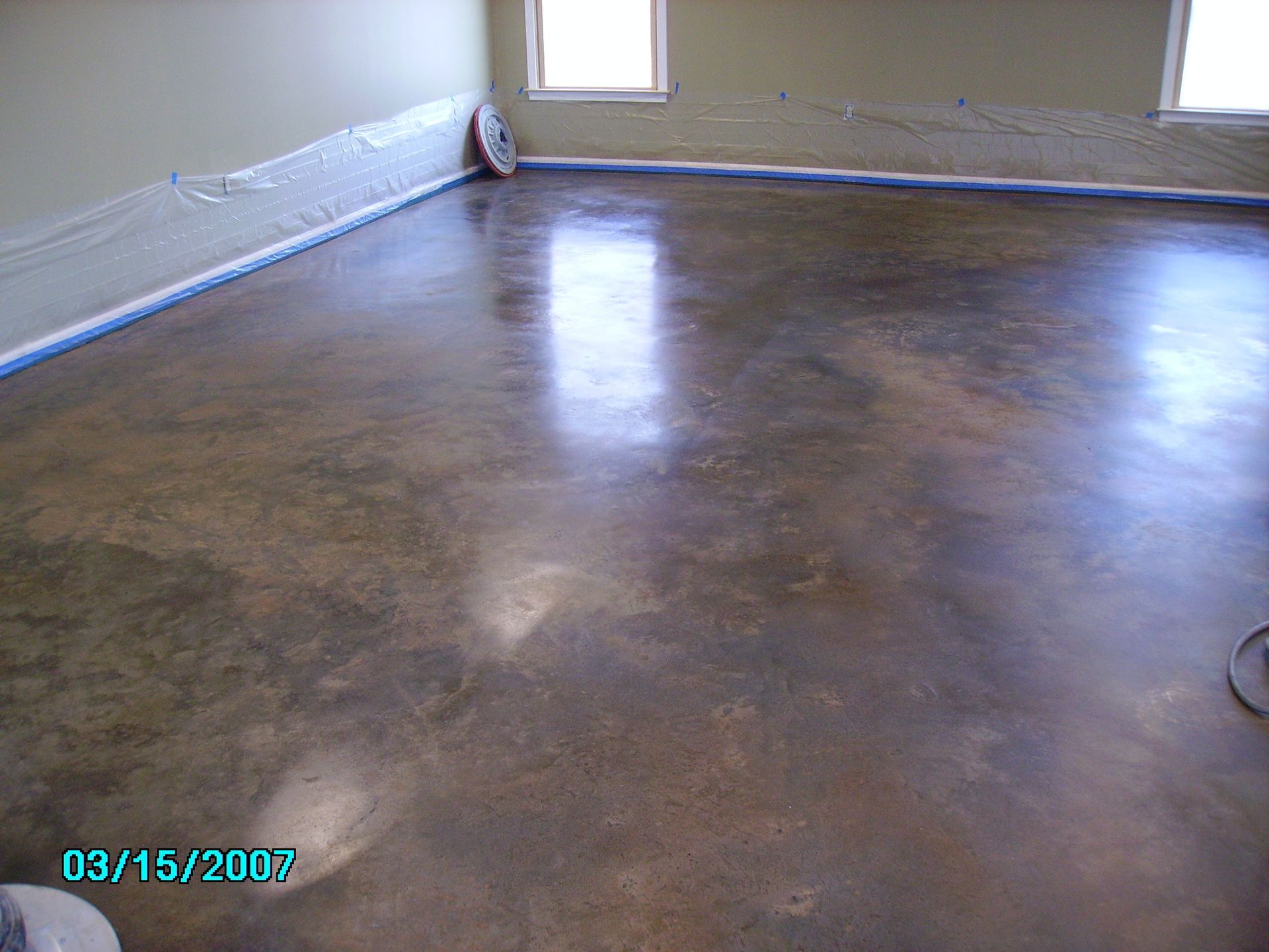 Polished concrete floor with variations of brown and gold tones, near windows and taped walls.