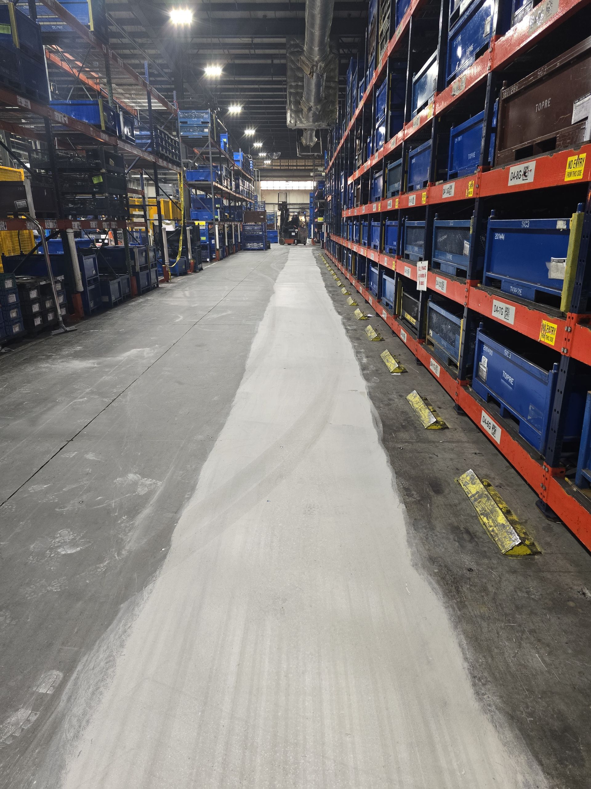 Warehouse aisle with a white, possibly chemical, spill down the center. Shelves of blue containers line the right side.
