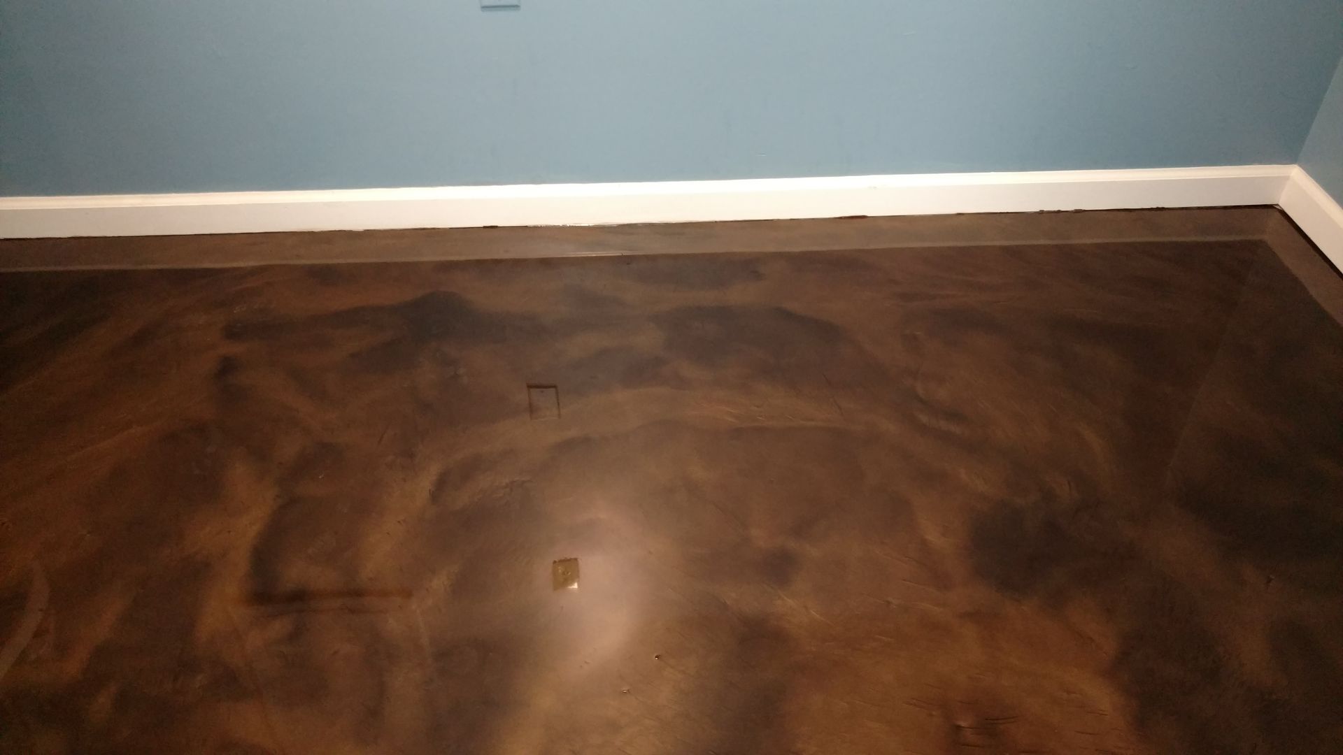Brown and gold epoxy floor with a flowing, marbled effect, against a blue wall and white baseboard.