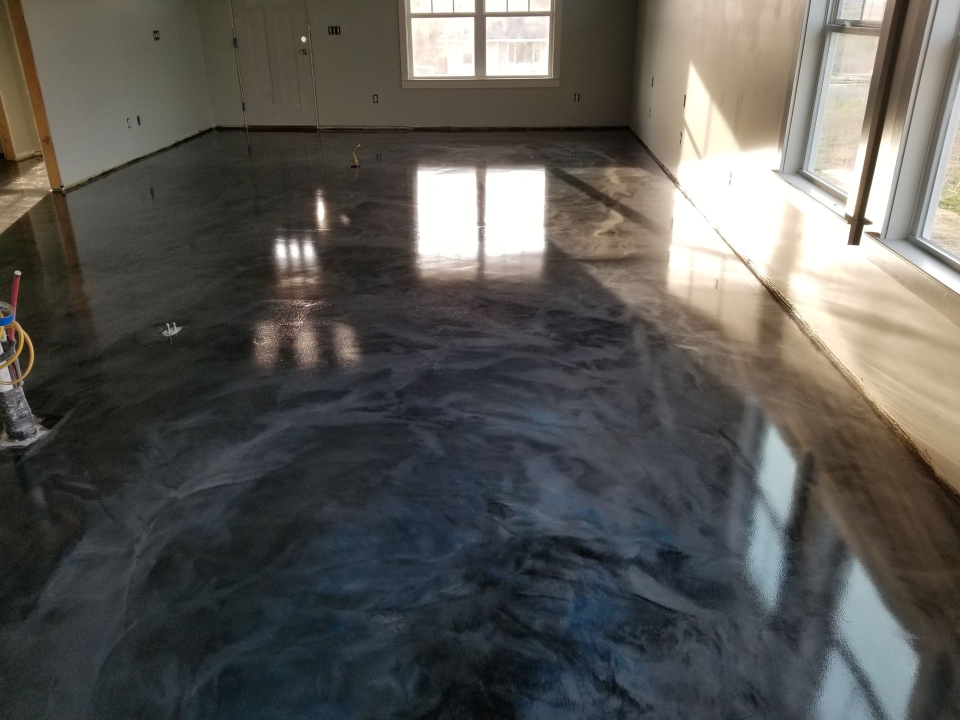 Metallic epoxy floor in a room, reflecting light from windows. The floor is a mix of dark grays and blues with a glossy finish.