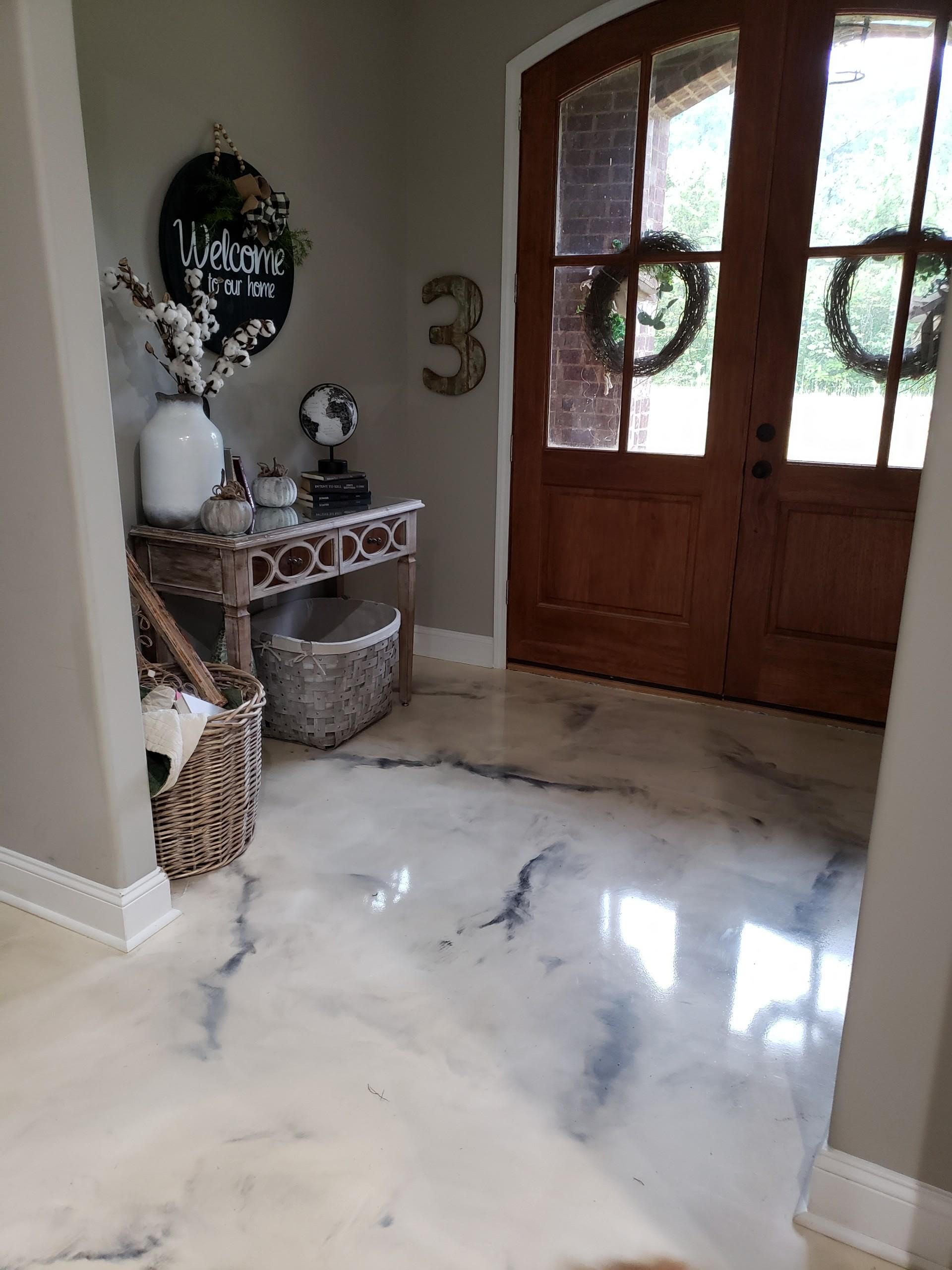 Entryway with shiny, marbled flooring, a wooden door with wreaths, and a console table decorated with a wreath and flowers.