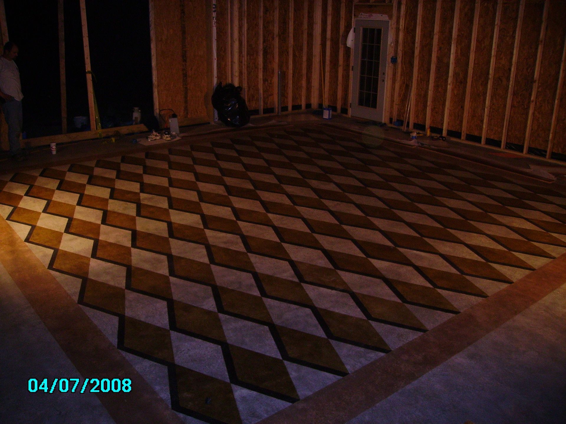Interior view of a room under construction with a diamond-patterned concrete floor in alternating tan and gray tones.