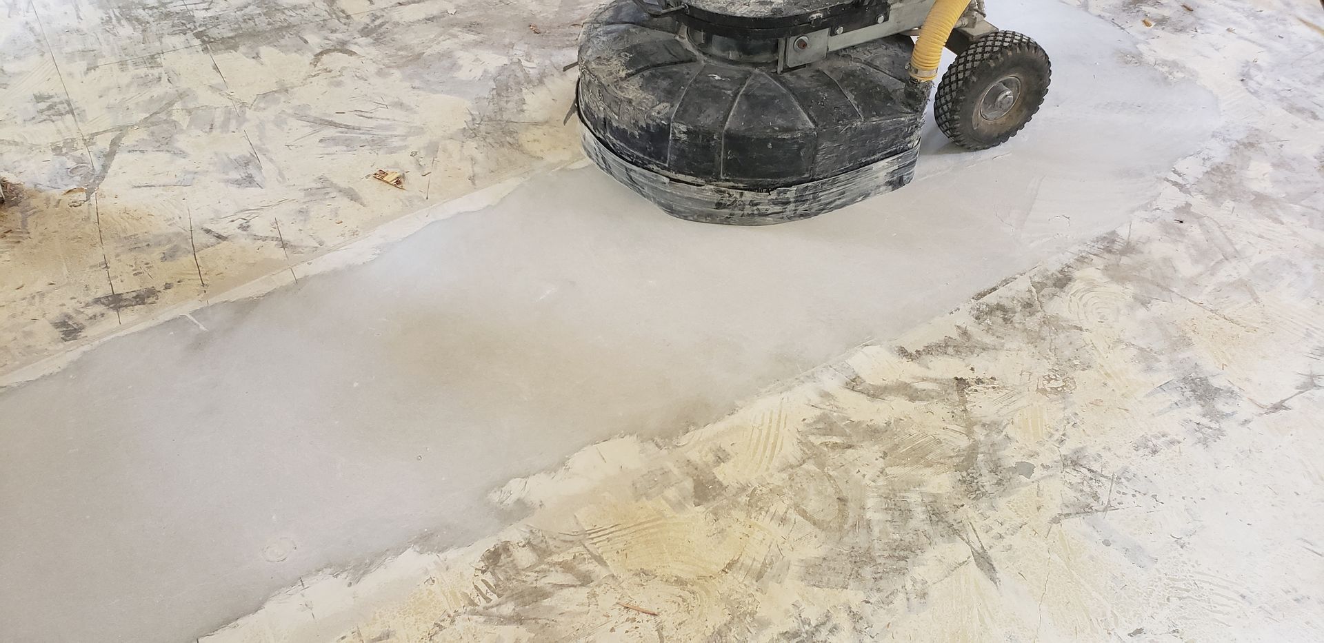 A machine grinding a concrete floor, creating a lighter-colored path amid the aged surface.