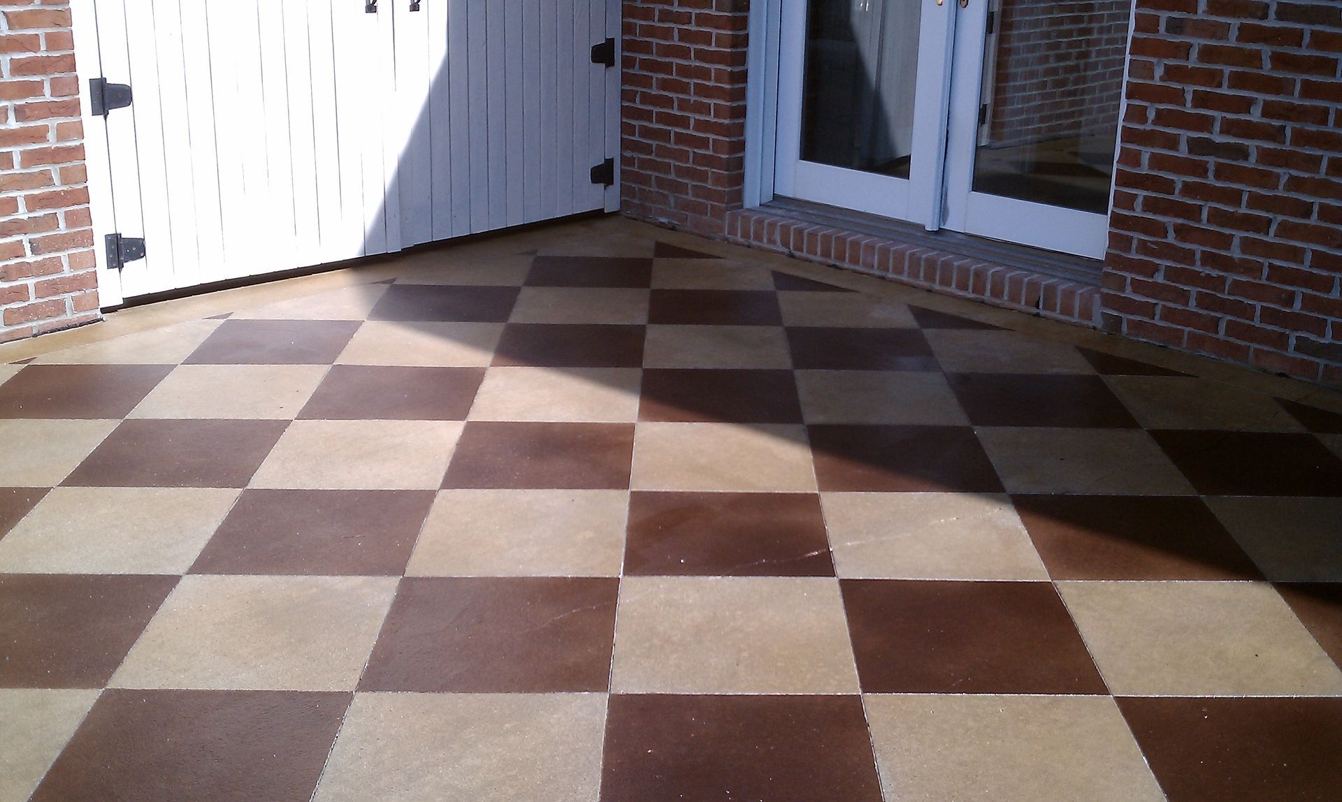 Checkered patio floor with brown and tan squares, next to a white door and brick wall.