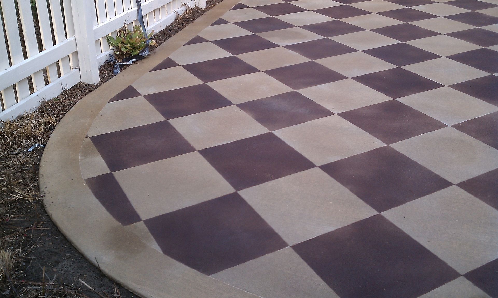 A checkered patio with a white fence in the background