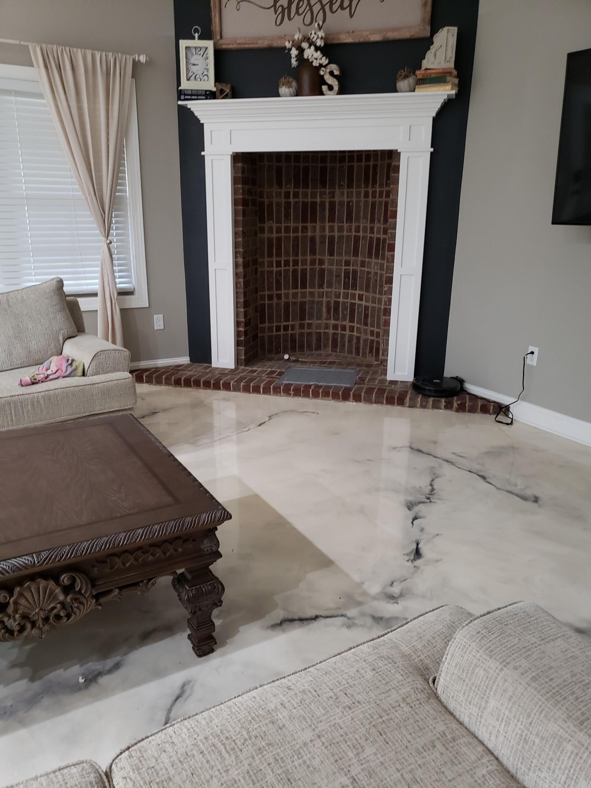 Living room with a decorative fireplace and a polished floor. The floor has a marbled design, and a coffee table is in the foreground.