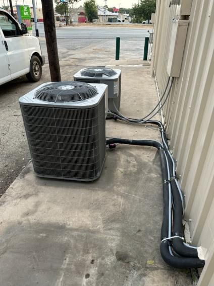 Two air conditioners are sitting on the sidewalk next to a building.
