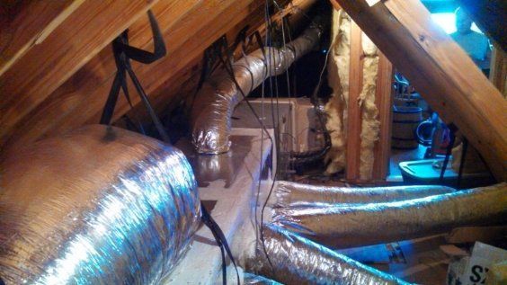 A bunch of ducts are hanging from the ceiling of an attic.