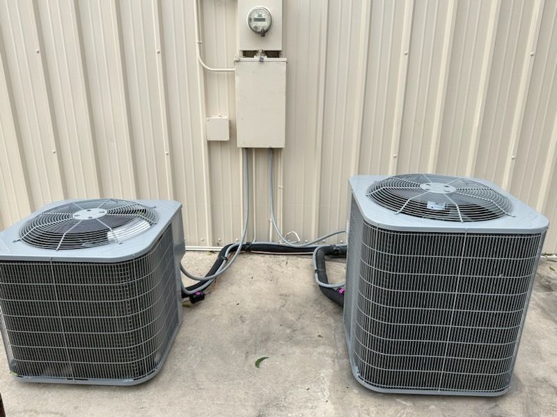 Two air conditioners are sitting next to each other on the side of a building.